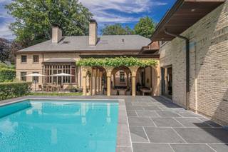 <p><span>Dit royale landhuis is gelegen op een ruim perceel van ruim 1 Ha met alle rust en privacy. De aangelegde parktuin biedt u een tennisterrein, ruime terrassen, verwarmd buitenzwembad etc. </span></p><p><span>Een uniek eigendom met vele mogelijkheden!</span></p><p><span> </span></p><p><span>Indeling</span></p><p><span>U betreedt de villa middels de dubbele voordeur naar een prachtige inkomhal met vide, gastentoilet met handenwasser en vestiaireruimte. Toegang naar de leefruimte alsook een doorgang naar de eetkamer. De ruime eetkamer heeft een ronde raampartij aan de voorzijde van de villa. Mede dankzij deze vorm is de eetkamer een zeer sfeervolle ruimte waar u een prachtig diner kunt organiseren. Via de tweede gang bereikt u vanuit de eetkamer ondermeer de leefkeuken , bar alsook de familyroom en zij-inkom. </span></p><p><span>De living bestaat uit een ruime woonkamer met gigantische open haard en vide naar de nachthal. Dankzij deze indrukwekkende plafondhoogte beschikt deze leefruimte ook over zeer hoge raampartijen met prachtig lichtinval en schitterend zicht op de tuin. Een tweede gedeelte van de living is de televisiekamer met eveneens een open haard. Aansluitend toegang tot een mooi ingericht kantoor. </span></p><p><span>De royale leefkeuken is mogelijk de belangrijkste ruimte van deze villa. Centraal gelegen in de woning en bereikbaar zowel vanuit de living alsook via de gang naar de eetkamer. Deze royale leefkeuken met open haard werd ingericht met een prachtige maatwerk keuken in eik en is voorzien van alle toestellen waaronder een prachtig fornuis. Vanuit de keuken ook toegang tot de tuin en het aangrenzende overdekte terras.</span></p><p><span>Voorts nog een tweede kantoor of familyroom met aparte inkom, een bar of aperitiefruimte, zij-inkom met mudroom alsook een aparte wellness met kleedruimtes, sanitaire voorzieningen en een sauna, dit alles grenzend aan het terras bij het zwembad. </span></p><p><span> </span></p><p><span>Eerste verdieping</span></p><p><span>Bereikbaar middels twee trappen alsook een lift heeft deze villa een zeer ruime eerste verdieping met drie gedeeltes; twee kinder-afdelingen met steeds twee slaapkamers welke een badkamer delen, een polyvalente kamer ( vijfde slaapkamer of hobbyruimte) en een zeer royale mastersuite bestaande uit een ruime slaapkamer, volledig ingerichte dressingkamer en een luxe afgewerkte badkamer. De separate waskamer is ingericht met kasten en aansluitingen voor de toestellen.</span></p><p><span> </span></p><p><span>Tweede verdieping</span></p><p><span>Middels de lift bereikt u de polyvalente zolder. Deze zeer grote ruimte biedt u alle mogelijkheden voor het realiseren van bijkomende slaapkamers, kantoor aan huis, fitness, alle mogelijkheden dus!</span></p><p><span> </span></p><p><span>Kelder</span></p><p><span>Vanuit de keuken bereikt u de kelder alwaar u eerst de wijnkelder met degustatieruimte betreedt om vervolgens nog verschillende bergruimtes en technische ruimtes te kunnen bereiken.</span></p><p><span> </span></p><p><span>Garages</span></p><p><span>De villa beschikt momenteel niet over een garage, echter is er de mogelijkheid tot bouwen van een vrijstaand garagegebouw of carport. Tevens is er een nog een oude conciërgewoonst welke kan worden veranderd naar – of vervangen door een garagegebouw. </span></p><p><span> </span></p><p><span>Tuin en buitenruimtes</span></p><p><span>De aangelegde parktuin is volledig omheind en voorzien van een aparte inrijpoort en uitgang. De tuin is voorzien van tuinverlichting alsook een beregeningsinstallatie. Tennisterrein op gravelbodem, ruim verwarmd zwembad met automatisch roldek, bijgebouw of tuinberging. </span></p><p><span> </span></p><p><span>Bijzonderheden</span></p><p><span>Deze zeer ruime villa werd gebouwd met gebruik van hoogwaardige materialen en voorzien van moderne luxe en comfort. De woning beschikt over een uitgebreid alarmsysteem, domotica, etc. </span></p><p><span> </span></p><p><span>Meer inlichtingen via ons kantoor</span></p>