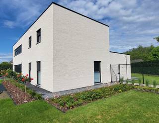 Instapklare nieuwbouwwoning (2025) op perceel van 1.167 m²<br />Op zoek naar een recent gebouwde woning die alles biedt wat een hedendaags gezin nodig heeft ?<br />Met een voorgevelbreedte van maar liefst 18 meter straalt deze eigendom ruimte en elegantie uit. Bij het betreden van de woning verwelkomt de stijlvolle inkomhal met gastentoilet u in een moderne leefomgeving. Via een doorgang met maatwerkkasten bereikt u de royale leefruimte waar woonkamer, eetplaats en open keuken naadloos in elkaar overvloeien. <br />De moderne keuken beschikt over een overvloed aan kastruimte en vormt het hart van de woning. Dankzij het grote schuifraam is de directe verbinding met het overdekte terras en de tuin. Aansluitend bevindt zich een praktische berging/wasplaats met afzonderlijke buitendeur.<br />Het gelijkvloers biedt daarnaast een comfortabele slaapkamer met dressing en een ruime badkamer met een ligbad als een stijlvolle inloopdouche. Ook de ruime garage met sectionaalpoort zorgt voor extra comfort en praktische opbergruimte.<br />Op de verdieping bevinden zich nog een tweede badkamer, een extra slaapkamer en twee volwaardige kamers. Hierdoor is deze woning uitermate geschikt voor grotere gezinnen of voor wie een thuisbureau of hobbyruimte wenst te creëren.<br />Buiten geniet u van een volledig aangelegde en omheinde tuin met een ruim tuinhuis van 25 m² en een overkapping van 15 m², beide voorzien van een tegelvloer. De automatische schuifpoort (4 m x 1,80 m) zorgt voor extra veiligheid en gebruiksgemak.<br />Ook op technisch vlak laat deze woning niets te wensen over. Ze is uitgerust met zonnepanelen, energiezuinige vloerverwarming, ventilatiesysteem D, elektrische rolluiken, domotica en een regenwaterrecuperatiesysteem.<br />Een bijkomende troef zijn de extra brede binnendeuren, die niet alleen een gevoel van ruimte creëren maar ook het wooncomfort verhogen voor minder mobiele bewoners.<br />Laat u verrassen door de ruimte, de afwerking en het wooncomfort van deze bijzondere eigendom.<br />bijkomende info 0477/241084.<br />
