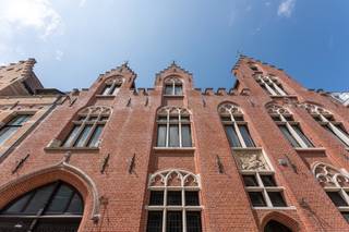 Dit uitzonderlijke herenhuis, 'Die Gulden Sporen', aan de Vlamingdam in Brugge, is een eerbetoon aan de Guldensporenslag. Gebouwd in 1896 door architect Oskar Dumon, combineert het pand geschiedenis met grandeur. Met circa 600 m² bewoonbare oppervlakte op een perceel van 550 m² is het een zeldzame stadsvondst.Het herenhuis beschikt over negen kamers, drie badkamers, twee keukens, een dubbele garage en een ruime zolder. Authentieke details zoals twaalf marmeren schouwen, mahoniehouten deuren en gerestaureerde salons tonen het vakmanschap. De gevel en het dak zijn in 2007 gerenoveerd.De strategische ligging nabij de Grote Markt en de Sint-Gilliskerk biedt een goede ontsluiting. De invloed van de Engelse stijl is zichtbaar in de architectuur, de Engelse tuin en het interieur. De dubbele salons vormen het hart van de woning, compleet met haarden en Versailles-parket, en lopen over op de zeldzame zuidgerichte stadstuin.