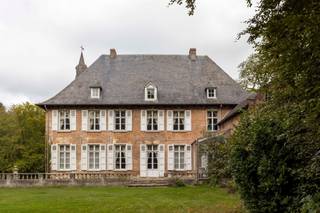 <p><span><span>Kasteelhoeve op uniek perceel in Tielen</span></span></p><p><span><span>In het groene landschap van de Kempen, vlak bij het recreatiedomein van De Hoge Rielen, bevindt zich het historische domein Tielenhof. Dit omgrachte kasteelgoed, waarvan de oorsprong teruggaat tot de 14de eeuw, ligt in het charmante dorp Tielen. Ondanks de rustige en landelijke setting geniet het domein van een vlotte bereikbaarheid: het treinstation van Tielen ligt op slechts enkele minuten wandelen, op ongeveer 800 meter afstand.</span></span></p><p><span><span>De geschiedenis van Tielenhof gaat eeuwen terug. Vermoedelijk liet Hendrik van Duffel rond 1350 op deze plek een kasteel optrekken dat lange tijd dienstdeed als residentie van de heren van Tielen. Doorheen de eeuwen wisselde het domein meermaals van eigenaar via huwelijken en erfenissen binnen verschillende adellijke families. Pas in 1958 werd het voor het eerst verkocht buiten deze kringen. Het kasteel kende meerdere verbouwingen: een ingrijpende aanpassing in 1830 transformeerde het tot een zomerresidentie, waarbij een deel van het oorspronkelijke middeleeuwse karakter verdween. Tijdens een restauratiecampagne in de jaren 1970 werden opnieuw historische elementen uit de 16de en 17de eeuw in ere hersteld, waaronder kruiskozijnen en de kenmerkende traptoren.</span></span></p><p><span><span>Vandaag vormt Tielenhof een karaktervol L-vormig geheel, opgebouwd in traditionele baksteen en zandsteen. De hoofdvleugel telt twee bouwlagen en wordt afgedekt met een steil schilddak. Het geheel wordt aangevuld met verschillende bijgebouwen, waaronder een barok koetshuis uit 1686 en een poortgebouw met houten ophaalbrug. De toegang tot het domein verloopt via de indrukwekkende Kasteeldreef: een circa 230 meter lange, gekasseide beukendreef die leidt naar het omgrachte terrein van ongeveer 1,7 hectare. Kastelen van dit type zijn uitzonderlijk in de Kempense regio en maken van Tielenhof een bijzonder stukje erfgoed.</span></span></p><p><span><span>De ligging midden in een natuurgebied maakt het domein uniek, maar vraagt tegelijk om een doordachte invulling. De bestemming blijft hoofdzakelijk residentieel, al zijn er diverse interessante mogelijkheden denkbaar: bijvoorbeeld een woonproject met mantelzorg of kangoeroewonen, het combineren van wonen met een kleinschalige horecazaak zoals een bistro of restaurant, of een cohousingconcept waarbij het karakter van één huishouden behouden blijft. Voor wie op zoek is naar een uitzonderlijke woonplek met geschiedenis, natuur en potentieel, biedt Tielenhof een zeldzame kans.</span></span></p><p> </p><p><span><span>Interesse? Bel ons nu voor het inplannen van een afspraak op 0489/89.49.74.</span></span></p>
