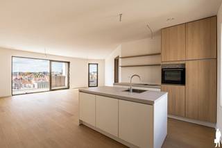 <p><strong>Residentie Tamboer – uw eigen ritme, midden in Turnhout</strong><br />De dag begint met licht dat langs twee kanten de leefruimte binnenvalt. U drinkt koffie met zicht op de stad, wandelt later naar de Grote Markt en komt ’s avonds thuis op een terras waar de laatste zon nog blijft hangen. Dat is het leven in dit penthouse van Residentie Tamboer: de stad dichtbij, met thuis alle ruimte om tot rust te komen.</p>
<p>De residentie dankt haar naam aan de tamboer, de trommelaar die het ritme aangeeft en de stoet voorgaat. Ook hier draait alles om ritme: de levendigheid van Turnhout wanneer u die opzoekt, en de rust van uw eigen plek wanneer u thuiskomt. Net binnen de ring woont u bij water, groen en wandelpaden, met de Grote Markt en het Stadspark op wandelafstand.</p>
<p><strong>Een terras dat mee leeft met uw dag</strong><br />Dit penthouse biedt 121 m² bewoonbare oppervlakte en maar liefst 46 m² aan terrassen. Het terras loopt rond het appartement en biedt plaats aan meerdere zithoeken: een tafel om buiten te eten, een plek om te lezen, of allebei. Dankzij de westelijke oriëntatie geniet u er van de namiddag- en avondzon, met de Turnhoutse skyline als decor. De lamellen bieden schaduw wanneer u daar behoefte aan heeft.</p>
<p>Binnen vormen de zithoek, eetruimte en stijlvolle keuken één open leefruimte. Grote ramen brengen aan twee zijden daglicht binnen en verbinden het interieur met het terras. De lichte eiken parketvloer geeft de leefruimtes een warme, tijdloze uitstraling.</p>
<p>Ook de drie slaapkamers hebben toegang tot de terrassen. De hoofdslaapkamer beschikt over een eigen badkamer. Voor de twee andere kamers is er een aparte douchekamer. Richt ze in als slaapkamers, bureau, dressing of hobbyruimte: de indeling geeft u de vrijheid om het appartement aan uw leven aan te passen.</p>
<p><strong>Groot in mogelijkheden, aangenaam in schaal<br /></strong>Residentie Tamboer combineert eigentijdse architectuur met warme materialen en groene gevels. De residentie is opgedeeld in compartimenten met elk een eigen trap en lift. Zo maakt u deel uit van een groter woonproject, terwijl u de gemeenschappelijke delen met slechts een beperkt aantal andere appartementen deelt.</p>
<p>Op het gelijkvloers is een ruime fietsenstalling voorzien. Uw wagen parkeert u in de afgesloten parkeerkelder.</p>
<p>De vraagprijs van het penthouse bedraagt € 429.900 exclusief kosten. Parkeerplaatsen zijn verkrijgbaar vanaf € 20.900 en bergingen vanaf € 4.500. Inclusief btw, registratierechten, notariskosten, één parkeerplaats en één berging bedraagt de totale aankoopprijs circa € 552.000.</p>
<p>Achter Residentie Tamboer staat DC Belgium, een ervaren Belgische projectontwikkelaar met aandacht voor woonkwaliteit en groen. Van uw eerste kennismaking tot de afwerking van uw appartement wordt u persoonlijk begeleid.</p>