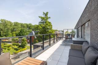 Dit ruim en lichtrijk penthouse van 147 m² (bruto) biedt uitzonderlijk veel wooncomfort in het centrum van Schulen. Met een prachtig groen uitzicht en twee grote terrassen van elk ruim 33,5 m² geniet u hier op elk moment van de dag van de zon en de rust. Het appartement beschikt over een royale leefruimte met een mooie open keuken en kookeiland, twee volwaardige slaapkamers, maatwerk, dressing en twee ruime badkamers. In de verkoop is bovendien een garagebox, een extra private autostaanplaats én een kelderberging inbegrepen. Op vlak van energie en techniek scoort de woning uitstekend met EPC label A (E-peil E47), vloerverwarming, zonnepanelen, domotica, verhoogde akoestische isolatie en een waterontharder. Het pand bevindt zich in een kleinschalige en uitstekend onderhouden residentie met een mooie tuin en bezoekersparking, rustig gelegen nabij de dorpskern, winkels en met een vlotte verbinding naar de snelwegen.