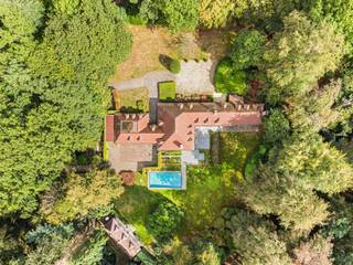 Verscholen in het groen van de gegeerde Bellevuedreef bevindt zich deze karaktervolle klassieke villa op een indrukwekkend parkdomein van ca. 1,4 hectare. Een eigendom waar ruimte, privacy en een bijzonder aangename woonbeleving samenkomen, omgeven door een volgroeide en zorgvuldig aangelegde tuin.<br /><br />De villa beschikt over ca. 575 m² bewoonbare oppervlakte en wordt aangevuld met een volwaardig gastenverblijf in het poolhouse, een afzonderlijke conciërgewoning, een inpandige garage voor drie wagens en een verwarmd buitenzwembad. De omvang van het domein, de volwassen begroeiing en de verschillende woon- en verblijfsfuncties maken van deze eigendom een bijzonder compleet geheel op een van de meest residentiële locaties van Schilde.<br /><br />Indeling gelijkvloers:<br />De centrale inkomhal met vestiaire en gastentoilet vormt het vertrekpunt van de woning en geeft toegang tot de verschillende leefruimtes.<br />De royale leefruimte omvat een zitkamer en eetkamer, aansluitend op een afzonderlijke studeerkamer. Daarnaast bevindt zich een ruim bureel met maatwerkkasten, waardoor ook professioneel of rustig thuiswerken perfect in de woning kan worden geïntegreerd.<br />Centraal in het dagelijkse leven staat de ruime leefkeuken, opgebouwd rond een gezellige ontbijtruimte met grote schuiframen naar het terras en de tuin. Het keukengedeelte met eiland is uitgerust met diverse inbouwtoestellen. Een praktische berging zorgt voor een tweede verbinding met de eetkamer, terwijl de bijkeuken met afzonderlijke zij-ingang bijkomende functionaliteit biedt.<br /><br />Eerste verdieping:<br />De nachthal leidt naar vier ruime slaapkamers, die elk over een eigen badkamer beschikken.<br />De mastersuite vormt een royaal privégedeelte met slaapkamer, dressing en badkamer. Daarnaast bevinden zich op deze verdieping een tweede ruime slaapkamer, een gastenkamer en een kinderkamer, telkens met een eigen badkamer.<br /><br />Vanuit de mastersuite is er via een tussengang en diensttrap verbinding met het gedeelte boven de garage.<br /><br />Conciërgewoning:<br />Boven de inpandige garage bevindt zich een afzonderlijk verblijfs- en conciërgegedeelte, bestaande uit een polyvalente leefruimte, slaapkamer en badkamer. Dit gedeelte leent zich uitstekend voor inwonend personeel, een au pair, familie of gasten.<br /><br />Kelder:<br />Via een natuurstenen trap is de kelderverdieping bereikbaar. Hier bevinden zich bijkomende bergruimtes, de technische installaties voor de woning en het zwembad en een sfeervolle wijnkelder.<br /><br />Poolhouse & gastenverblijf:<br />Aan het verwarmde zwembad bevindt zich een royaal bijgebouw, architecturaal afgestemd op de hoofdwoning. Het poolhouse werd ingericht als een volwaardig zelfstandig gastenverblijf met woonkamer, keuken, slaapkamer en badkamer.<br />Samen met de omliggende terrassen en het zwembad ontstaat hier een bijzonder aangename omgeving voor ontspanning, familie en gasten, met een grote mate van privacy ten opzichte van de hoofdwoning.<br /><br />Bijzonderheden:<br />- Uitzonderlijk parkdomein van ca. 14.433 m²<br />- Volledig omheind domein met maximale privacy<br />- Volgroeide tuin met uitgestrekte gazons en volwassen bomen<br />- Regelmatig onderhouden en verder opgefrist<br />- Verwarmd buitenzwembad<br />- Volwaardig poolhouse ingericht als zelfstandig gastenverblijf<br />- Afzonderlijk conciërge- of personeelsverblijf<br />- Inpandige garage voor drie wagens<br />- Verschillende ruime terrassen rondom de woning<br />- Uitgebreide tuinverlichting<br />- Alarm- en camerabewaking<br /><br />Een bijzonder compleet residentieel domein waar ruimte, discretie en groen centraal staan, op een van de meest gewaardeerde locaties van Schilde.