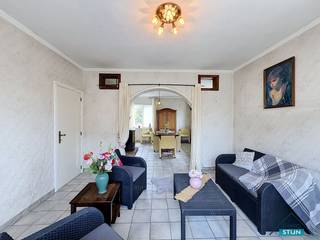 Deze ruime woning geniet van een vlotte verbinding met de E403 en het openbaar vervoer en ligt bovendien in de nabijheid van diverse winkels. Via de inkomhal bereik je de lichtrijke woonkamer, de keuken en de eerste verdieping. De woonkamer biedt voldoende plaats voor een gezellig zitgedeelte en een eetkamer. De naastgelegen keuken is ingericht met een geïnstalleerde keuken en geeft toegang tot de kelder en een tweede woonkamer. Vanuit deze tweede woonkamer bereik je de wasberging met aansluitend een badkamer, voorzien van een douche en lavabomeubel. Via de hal kom je bij het afzonderlijke toilet. Op de eerste verdieping bevinden zich de nachthal, een tweede badkamer en drie slaapkamers. Deze badkamer is uitgerust met een ligbad, lavabo en toilet. Mits het opnieuw plaatsen van een vaste trap kan ook de tweede verdieping opnieuw volwaardig worden benut. Hier werden nog twee extra slaapkamers ingericht. Naast de woning loopt een oprit met poort die toegang geeft tot de ruime garage en de tuin. Buiten is er bovendien een kleine werkplaats, ideaal voor wie graag klust of extra bergruimte zoekt. Achteraan de tuin bevinden zich nog een moestuin en een kippenhok. Een ruime woning met heel wat mogelijkheden, zowel binnen als buiten. (sted.inl.: in aanvraag)