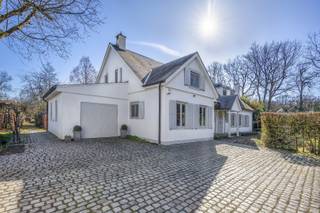 Bij het betreden van de woning komt u in een ruime inkomhal met karaktervolle Bourgondische tegelvloer, die meteen de warme sfeer van de woning zet. Aan de rechterzijde bevindt zich de gezellige leefruimte met authentieke zitput, een ideale plek om in alle comfort te ontspannen.<br /><br />Achteraan de woning bevindt zich een ruime, volledig uitgeruste keuken met Miele-toestellen, die naadloos aansluit op de lichtrijke veranda. Deze veranda is voorzien van airconditioning en biedt een prachtig uitzicht op de fraai aangelegde tuin met vijver, waardoor binnen en buiten harmonieus in elkaar overvloeien.<br /><br />Op het gelijkvloers vindt u verder nog een ruime bureauruimte aan de voorzijde van de woning, perfect geschikt als praktijkruimte of voor wie comfortabel van thuis wil werken. Daarnaast beschikt de woning op dit niveau over een slaapkamer met ensuite badkamer, een praktische wasruimte en een inpandige garage met automatische poort.<br /><br />De verdieping omvat vier slaapkamers. Twee slaapkamers zijn momenteel met elkaar verbonden, maar kunnen eenvoudig opnieuw afzonderlijk gebruikt worden. De derde slaapkamer is bijzonder ruim en de master bedroom beschikt over een eigen badkamer met ligbad en douche, evenals een aparte dressing. De trappenhal is voorzien van ingemaakte kasten, wat zorgt voor een overvloed aan praktische bergruimte.<br /><br />Ook buiten heeft deze eigendom heel wat troeven. De volledig omheinde tuin biedt optimale privacy en is vooraan voorzien van een dubbele garage met daarboven een polyvalente ruimte, die volledig naar eigen wensen kan worden ingericht. De mooi aangelegde vijver en de uitrit achteraan het perceel maken het geheel compleet.<br /><br />Het perceel van 4.974 m² bestaat uit twee bouwgronden, waardoor het achterste gedeelte in de toekomst eventueel kan worden benut voor de bouw van een extra woning. Met een straatbreedte van meer dan 50 meter geniet u bovendien van een uitzonderlijk ruimtelijk gevoel.<br /><br />De woning is uiterst rustig gelegen aan de rand van het Zoerselbos, een ideale omgeving voor wandel- en fietsliefhebbers. Tegelijk bevindt u zich op korte afstand van de op- en afrit van de E34, wat zorgt voor een vlotte bereikbaarheid. Een unieke combinatie van rust, ruimte en bereikbaarheid.