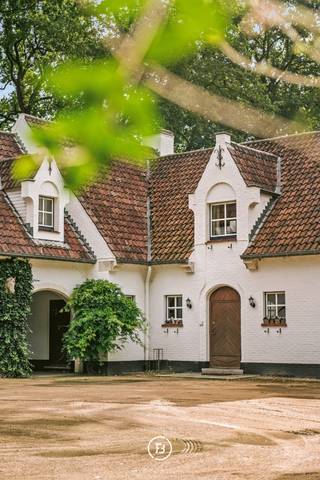 Dit gezellige landhuis is gelegen op een uitzonderlijk groen domein van circa 2 hectare. Met een royale woonoppervlakte van ca. 420 m², een karaktervolle architectuur en een prachtige parkomgeving biedt deze eigendom een unieke combinatie van ruimte, privacy en authenticiteit.<br /><br />De woning werd gebouwd in 1973 en ademt de sfeer van een klassiek herenhuis. Authentieke materialen werden doorheen de woning zorgvuldig bewaard. Zo zorgen onder meer de eiken deuren en de karaktervolle vloeren met kerkelijke tegels, stijlvol omzoomd met eikenhout, voor een warme en tijdloze uitstraling.<br /><br />Met ca. 420 m² woonoppervlakte beschikt het pand over bijzonder royale leefruimtes en tal van mogelijkheden voor wie op zoek is naar een ruime gezinswoning of een eigendom waar wonen, werken en hobby's gecombineerd kunnen worden. Daarnaast zijn er een grote kelder en een zolder aanwezig, die extra ruimte bieden voor berging, hobby's of andere invullingen.<br /><br />Ook op technisch vlak beschikt de woning over comfortabele voorzieningen, waaronder verwarming op gas, dubbele beglazing en airconditioning in zowel de keuken als de grote slaapkamer. Twee garages met automatische poorten bieden plaats aan wagens en bijkomende opslag. Verder is er een afzonderlijke houtopslag voorzien.<br /><br />De absolute blikvanger is het terrein van circa 2 hectare in parkgebied. De uitgestrekte, verzorgde tuin met fruitbomen werd oorspronkelijk aangelegd als boomgaard en creëert een uitzonderlijk groene en landelijke woonomgeving.<br /><br />Een charmant bruggetje over de sloot herinnert aan de historische eilandstructuur van het perceel en versterkt het unieke karakter van het domein. Het terrein is omheind en beschikt over een waterput en een tweede uitgang richting de hoofdweg.<br /><br />Een karaktervol landelijk herenhuis met uitzonderlijk veel ruimte, zowel binnen als buiten, op een groen domein van circa 2 hectare.