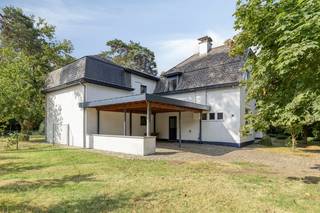 Instapklare, maar op te frissen villa met veel potentieel en uitzonderlijke ligging op mooi perceel(18a14). Omwille van de grote bewoonbare oppervlakte(350m2) en aparte indeling kan deze eigendom bewoond worden als gezinswoning, kangoeroewoning of gebruikt worden voor een vrij beroep in combinatie met woonst.<br /><br />Het goed werd door de jaren verbouwd/uitgebreid(steeds met vergunning). In 1987 werd de leefruimte rechts vergroot, in 1997 werd aan de achterzijde een extra leefruimte met slaapkamer en badkamer toegevoegd en in 2003 werd de eerste verdieping(houten buitengevel) uitgerust met een extra slaapkamer.<br /><br />Momenteel bestaat de woning uit: een inkomhal, ruime leefruimte (met bar, zithoek en openhaard), een bureau, ruime berging, uitgeruste hedendaagse keuken met doorgang tot het overdekt terras voorzien van buitenkeuken, tweede leefruimte en badkamer op het gelijkvloers. Op de eerste verdieping bevinden zich 6 slaapkamers( de meeste met sanitair), een tweede badkamer en apart toilet.<br /><br />Verder beschikt deze woning over een ruime tuinberging, een kelder, een carport voor twee wagens en een afgewerkte zolder. De woning is uitgerust met zonnepanelen, centrale verwarming (condesatieketel op aardgas) en op één van de slaapkamers is airco voorzien.<br /><br />We werken met een vanaf prijs waarbij alle biedingen mogelijk zijn en aan de eigenaar voorgelegd worden.<br /><br />Voor meer informatie of een bezoek ter plaatse –> ken@immovos.be of 0477/ 29 72 50