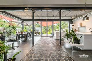 In het landelijke Letterhoutem, deelgemeente van Sint-Lievens-Houtem, bevindt zich deze vrijstaande villa met een uitgesproken industriële architectuur. De woning werd ontworpen met aandacht voor duurzaamheid én functionaliteit en staat op een indrukwekkend perceel van 5.275 m². Een bijzondere eigendom voor wie houdt van architectuur en ruimte, maar ook ideaal voor wie wonen en werken wil combineren. De open inkomhal met gastentoilet vloeit over in de indrukwekkende leefruimte met open keuken. Samen vormen ze maar liefst 135 m² aan open woonruimte. Grote raampartijen zorgen voor veel natuurlijk licht en een prachtig contact met de aangelegde tuin en het terras. De volledig ingerichte keuken beschikt over alle hedendaagse toestellen. Een bijzondere eyecatcher is de goederenlift in de leefruimte. Deze past perfect binnen de industriële architectuur en is tegelijk bijzonder praktisch om materiaal en spullen naar de verdieping te brengen. Verder bevindt zich op het gelijkvloers een zeer ruime berging en wasplaats met afzonderlijke toegang. Ook deze indeling biedt interessante mogelijkheden voor wie privé en professioneel gebruik onder één dak wil combineren. Op de eerste verdieping bevindt zich de master bedroom, momenteel ingericht op de vide en voorzien van een ensuite badkamer. Daarnaast zijn er nog twee ruime slaapkamers, een tweede badkamer en een afzonderlijke wasplaats/berging. Ook technisch werd aan comfort gedacht. De woning beschikt over 6 airco-units en twee regenwaterputten van elk 6.000 liter. Buiten zet het ruimtegevoel zich verder. De aangelegde tuin beschikt over een royaal terras en een ruime garage van 33 m². Achteraan bevindt zich een groot stuk weideland. Dankzij het totale perceel van 5.275 m² is deze eigendom dan ook bijzonder interessant voor dierenliefhebbers, hobbyisten of mensen die simpelweg dromen van veel eigen buitenruimte. Een unieke villa waar industriële architectuur, ruimte, wonen en werken op een bijzondere manier samenkomen. Interesse? Vraag uw bezoek aan via Immo Francois en ontdek ter plaatse de architectuur en mogelijkheden van deze eigendom.<br /><br />