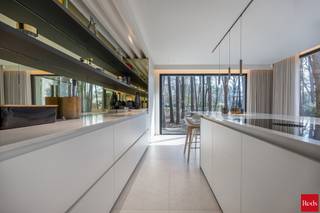 <p>Een villa die fluistert met het bos — overal waar u kijkt, de natuur.</p>
<p>In het hart van het gegeerde Koningshof in Schoten, discreet gelegen in een doodlopende straat, bevindt zich deze uitzonderlijke villa. Een plek waar stilte, privacy en natuur de hoofdrol spelen, op wandelafstand van het centrum, scholen en sportvoorzieningen. Hier woont u omringd door groen, zonder in te boeten aan bereikbaarheid.<br />De woning is volledig georiënteerd naar de tuin en het fenomenale uitzicht op het omliggende groen. Vanuit elke kamer kijkt u op een tapijt van dennenbomen. Het gevoel om in de natuur te wonen is hier geen belofte — het is uw dagelijkse realiteit. Rust, privacy en ruimte vloeien hier naadloos samen.</p>
<p><strong>Gelijkvloers- elegantie en leefkwaliteit in harmonie<br /></strong>Bij het betreden van de villa wordt u verwelkomd in een indrukwekkende inkomhal met hoge plafonds, ingebouwde vestiairekasten en gastentoilet — een eerste indruk die onmiddellijk de toon zet.<br />De leefruimte ademt warmte en verfijning, met een sfeervolle zithoek voorzien van gashaard, een stijlvolle bar en maatwerkkasten die perfect opgaan in het geheel. Grote raampartijen met adembenemend uitzicht op de bos, verbinden interieur en natuur naadloos met elkaar en geven rechtstreeks toegang tot het terras en de tuin.<br />De keuken vormt het absolute hart van de woning en is uitgevoerd met hoogwaardige materialen en de meest moderne, geïntegreerde toestellen. Aansluitend bevindt zich een elegante eetruimte weeral met panoramisch zicht op het groen.<br />Op subtiele wijze werd in de leefruimte een bureauruimte met ingemaakte kasten geïntegreerd, ideaal voor thuiswerk. Daarnaast is er een polyvalente ruimte die kan worden ingericht als speelkamer of extra kantoor.<br />Het zonovergoten terras sluit harmonieus aan op de leefruimtes en vormt een natuurlijke overgang naar de tuin — de perfecte plek om in alle rust te genieten van de natuur. Verder beschikt de woning over een dubbele garage en een kelder met kruipruimte onder het volledige gebouw.</p>
<p><strong>Eerste verdieping – een private suite op uitzonderlijk niveau<br /></strong>Via de elegante trap bereikt u de eerste verdieping, waar een overloop in visgraatparket toegang geeft tot vier slaapkamers.<br />De master suite van liefst ca. 100 m² vormt een private wereld op zich. Een royale slaapkamer vloeit over in een op maat gemaakte dressing en leidt naar een luxueuze badkamer van uitzonderlijk niveau, uitgerust met vrijstaand ligbad, dubbele regendouche en hoogwaardig kraanwerk. Het panoramische uitzicht op de omliggende dennenbossen maakt deze ruimte werkelijk uniek.<br />De drie overige slaapkamers (ca. 22 m², 18 m² en 15 m²) zijn eveneens afgewerkt met maatwerkkasten en genieten allen van een prachtig zicht op het groen.<br />Ook de kinderen beschikken over een stijlvolle badkamer met inloopdouche, dubbele lavabo en toilet. Bovendien bestaat de mogelijkheid om een derde badkamer te creëren.<br /><br /><strong>TECHNOLOGIE & DUURZAAMHEID <br /></strong>Het geheel is afgewerkt met de <strong>finest materialen</strong> en uitgerust met de <strong>meest geavanceerde technieken:</strong> zonnepanelen met thuisbatterij, geothermische warmtepomp, ventilatiesysteem type D, vloerverwarming (verwarmen én koelen), domotica, alarmsysteem en camerabewaking. Kortom — een uiterst energiezuinige en toekomstgerichte thuisbasis met EPC-label A+.</p>
<p>Deze villa is geen gewone woning, maar een totaalbeleving waar privacy, ruimte en luxe harmonieus samenkomen in een uitzonderlijk groene en discrete setting.<br /><br />Voor meer informatie of een bezichtiging van deze uitzonderlijk villa neem gerust contact met Stephanie of Sigalit via stephanie@reds.be of sigalit@reds.be.</p>
<p><br /><br /></p>