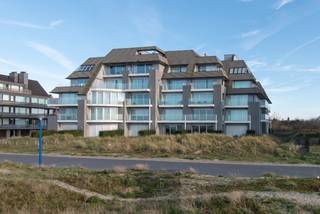 Uitzonderlijk doorloop-appartement in de prestigieuze residentie The Sanctuary, gelegen op de eerste lijn van het strand van Groenendijk te Oostduinkerke, op de grens met Nieuwpoort-Bad. Deze gegeerde ligging, pal aan zee en vlak bij surfclub Windekind, combineert rust, natuur en strandbeleving op een unieke manier.<br />De residentie werd in 1988 ontworpen door de gerenommeerde architect Marc Corbiau, wat zich vertaalt in een tijdloze architectuur met een sterke focus op licht, ruimte en zichtlijnen. Het appartement beschikt over een netto woonoppervlakte van 113 m² en maar liefst 35 m² aan terrassen. Vooraan bevindt zich een aangenaam terras met zicht op de duinen en de zee, terwijl aan de achterzijde een ruim en zonnig terras zorgt voor extra buitenruimte en privacy.<br />Het lichtrijke appartement is praktisch en comfortabel ingedeeld. Via de inkomhal met vestiaire en apart toilet betreedt u de leefruimte. De halfopen keuken is uitgerust met alle nodige apparatuur en sluit mooi aan op de ruime woonkamer, die dankzij grote raampartijen uitgeeft op het terras aan de voorzijde.<br />De nachthal biedt plaats aan een handige slaaphoek met ingemaakte kasten. Verder beschikt het appartement over een badkamer met dubbele wastafel, ligbad en toilet.<br />De eerste slaapkamer is voorzien van twee enkele bedden en een eigen badkamer met wastafel, douchecel en toilet. De tweede slaapkamer is voorzien van een tweepersoonsbed. Beide slaapkamers geven uit op het grote zuidgerichte terras aan de achterzijde.<br />Als extra troef is er een privatieve kelderberging inbegrepen en bestaat de mogelijkheid tot aankoop van een garagebox in de residentie. Daarnaast beschikt het gebouw over een gemeenschappelijke fietsenberging en een surfberging met douche, ideaal voor wie optimaal wil genieten van zee, strand en watersport.<br />Dankzij de unieke ligging aan het strand van Groenendijk, de royale oppervlaktes en de karaktervolle architectuur vormt dit appartement een bijzonder aantrekkelijke opportuniteit, zowel als tweede verblijf aan zee als voor wie op zoek is naar een ruim appartement op een absolute toplocatie. EPC: 450 kWh/m². Vraagprijs: 895000€