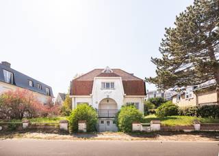 Met trots stellen wij u deze te renoveren villa voor, gelegen in de Dorlodotlaan te Koksijde-Bad.<br /><br />Deze karaktervolle villa geniet van een absolute bevoorrechte ligging: pal tegen de Schipgatduinen en op amper 100 meter van het strand. De woning vraagt een grondige, volledige renovatie — maar wie bereid is die stap te zetten, krijgt er een uitzonderlijk gegeven voor terug: een ruime, vrijstaande villa in een van de meest gewilde straten van de kust, volledig naar eigen inzicht en smaak in te richten.<br /><br />De woning is gelegen op een perceel van 530 m² en heeft een bewoonbare oppervlakte van 228 m². Ze werd als volgt ingedeeld:
<ul>
	<li>Benedenverdieping: ruime inkomhal | zitruimte | grote leefruimte | keuken | berging | toegang tot grote kelder | garage</li>
	<li>Tussenverdieping: badkamer | toilet | berging</li>
	<li>Eerste verdieping: vijf slaapkamers</li>
	<li>Tweede verdieping: twee slaapkamers</li>
</ul>
<br />In totaal beschikt de villa over ZEVEN slaapkamers, wat de woning bijzonder veelzijdig maakt: een grote gezinsvilla aan zee, een bed &amp; breakfast, of een volwaardig renovatieproject met toekomstvisie. Het ruime perceel biedt bovendien interessante bouwmogelijkheden — informeer bij de bevoegde stedenbouwkundige dienst naar de mogelijkheid tot het optrekken van een koppelvilla.<br /><br />Bent u op zoek naar een volwaardig renovatieproject op een toplocatie aan de kust? Contacteer ons vandaag nog voor een bezoek ter plaatse.