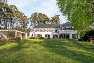 <p>Quares - TREVI Groep presenteert :<br />Voor deze knappe eigendom klinken superlatieven te bescheiden. Het is werkelijk indrukwekkend, fenomenaal, magnifiek! Voor wie houdt van discretie, rust, luxe en privacy.</p>
<p>Na een 70m lange oprijlaan verschijnt een elegante gevel die je onmiddellijk doet dromen: je waant je in de Hamptons, New York. De recent vernieuwde gevelbekleding doet de woning schitteren in haar nieuwe jasje. Een lang bordes nodigt je uit om de woning te ontdekken.</p>
<p>Binnen kijk je je ogen uit in de royale inkomhal met keizerlijke trap, die naar de bibliotheek en slaapvertrekken leidt.</p>
<p>GELIJKVLOERS:</p>
<p>In de rechtervleugel bevinden zich de dubbele garage met berging, vestiaire, en de logeerkamer met en suite gastenbadkamer.</p>
<p>In de linkervleugel ligt de bureauruimte waar het rustig werken is, en die ruim genoeg is om klanten op aangename wijze te ontvangen; en een gastentoilet.</p>
<p>Aan de achterzijde bevindt zich de gigantische leefruimte met keuken: het kloppende hart van de woning, met een adembenemend zicht op de tuin.</p>
<p>Dit deel is bijzonder stijlvol vernieuwd, met een hedendaagse look & feel en hoogwaardige materialen. Een grote gashaard, gezellige zitput, gimmicks zoals een verdwijnend raam en doorkijk naar de keuken, maken dat deze ruimte op verschillende momenten van de dag anders aanvoelt. Het grote panoramische raam is als een landschapsschilderij, maar dan van de eigen tuin. De keuken is volledig geëquipeerd en wordt geflankeerd door een enorm overdekt terras, waardoor het binnen-buitengevoel compleet is. Dit is een woning waar je kan genieten, en je graag veel tijd in wil doorbrengen.</p>
<p>VERDIEPING:</p>
<p>Linkervleugel: hier bevindt zich de grootste badkamer, een behoorlijk futuristisch ontwerp met centraal element waarrond de verschillende functies zich bevinden: ruime douche, hoekbad, dubbele lavabo, omkleedhoek. Aansluitend bevindt zich een praktische wasplaats, strijkruimte en apart toilet.</p>
<p>Een dressing leidt naar de comfortabel ruime master bedroom met zicht op de tuin, die naar een tweede open dressing of extra slaapkamer leidt. Ernaast bevindt zich een fitnessruimte die een derde slaapkamer kan zijn.<br /><br />In de rechtervleugel bevinden zich 2 prachtige ruime slaapkamers met mezzanine - een droom voor vele tieners – en een derde badkamer met ligbad en douche completeert het geheel.</p>
<p>Samen komen we op 6 slaapkamers in het totaal, 5 boven en 1 beneden, plus een dressing boven en bureau beneden. Ideaal voor wie ruim wil wonen, samengesteld gezin, werken & wonen, B&B en wonen, etc.</p>
<p>KELDER</p>
<p>Uiterst praktisch is de enorme kelder die deels verwarmd is, met hobbyruimtes, wijnkelder en opslagruimtes. Verder is er nog een kruipkelder.</p>
<p>TUIN:</p>
<p>In de tuin aansluitend aan de oprit, bevindt zich een bijgebouw met aparte fietsenberging, berging voor alle tuinonderhoudsmaterialen, en ruimte voor sport en ultieme ontspanning: een zwemspa met jetstream & onderwaterloopband, en een heerlijke jacuzzi. Wellness in eigen tuin. De tuin zelf is een prachtig glooiend gazon met zuid-zuidwest oriëntatie, omzoomd met struiken, bloemen en grote bomen. Mooi aangelegd èn beperkt in onderhoud zodat je er ook echt van kan genieten.</p>
<p>Halverwege de tuin loopt het hoofdperceel over in 2 percelen bouwgrond (85B en 85C op het bijgevoegde plan), die mee aangekocht kunnen worden aan respectievelijk 300.000EU en 325.000EU, maar die niet allebei absoluut noodzakelijk zijn om het weidse aspect te behouden.</p>
<p>Technisch is deze woning uitgerust met warmtepompen, airco, dak- en muurisolatie, hoogrendementsglas, alarm en camera’s, domotica, een conforme state-of-the-art elektrische installatie, en mèt een EPC A, wat zeer uitzonderlijk is voor dit type woning en uiteraard een enorme troef!</p>
<p>Geïnspireerd en klaar om deze droomwoning te ontdekken? Maak dan een afspraak met Tinne op 0477 60 21 99 of tinne.schotsmans@quares.be</p>