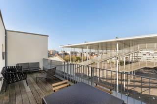 <p>Een ruim en lichtrijk duplex-appartement met een uniek karakter, gelegen op de bovenste verdiepingen van een modern gebouw. Deze woning combineert stedelijk wooncomfort met een opmerkelijk terras en een weids panoramisch uitzicht over de stad.</p>
<p>De woonkamer op houten vloer met kamerhoge raampartijen biedt ruimte voor zowel een comfortabele zithoek als een volwaardige eethoek. Aansluitend aan de eethoek bevindt zich een separate, ingerichte keuken met ingebouwde apparatuur. Een raam geeft ook hier zicht op de stad — koken wordt een aangenaam moment.<br />Op de leefverdieping bevindt zich een eerste ruime slaapkamer met aansluitend badkamer. Een stalen trap met houten treden verbindt de woonverdieping met de bovenste verdieping waar zich twee bijkomende slaapkamers en een badkamer bevinden. <br /><br />Wie droomt van buitenleven in de stad, vindt hier zijn gading. Het ruime terras biedt een panoramisch zicht over het Theaterplein, compleet met zithoek en eettafel. De perfecte plek voor een aperitief bij zonsondergang of een ontspannen weekendochtend.</p>
<p>Het gebouw is uitstekend gelegen in de nabijheid van de Antwerpse binnenstad, winkels, horeca en openbaar vervoer. <br />Twee autostaanplaatsen worden te koop aangeboden voor 50.000 euro per plaats.</p>