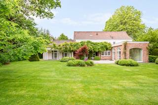 Op een absolute toplocatie in het gegeerde Schilde-Bergen, rustig gelegen nabij St. Ludgardis en omgeven door mature groenaanplantingen, bevindt zich deze perfect onderhouden klassieke villa op een mooi perceel van ca. 2.162 m². De woning biedt royale leefruimtes, 6 slaapkamers, 4 badkamers en een sfeervol bijgebouw achteraan in de tuin. Dankzij de zuidgerichte oriëntatie en de hoogwaardige afwerking is dit een unieke eigendom op één van de meest gegeerde lanen van Schilde.<br /><br />Indeling gelijkvloers:<br />De elegante inkomhal met natuurstenen vloer, vestiaire met gastentoilet en witgelakte trappartij geeft toegang tot de verschillende leefruimtes.<br />De opeenvolging van leefruimtes creëert een heerlijk ruimtelijk gevoel: een zitkamer met openhaard, een aparte eetkamer en een 3e royale leefruimte met grote raampartijen rondom, telkens met zicht op de tuin en directe toegang tot de terrassen.<br /><br />De volledig uitgeruste keuken in tijdloos wit beschikt over een kookeiland, veel kastruimte en kwalitatieve toestellen (o.a. Miele). Aansluitend bevinden zich een praktische voorraadruimte, een ruime wasplaats met ingemaakte kasten, een extra gastentoilet en toegang tot de inpandige dubbele garage.<br /><br />Eerste verdieping:<br />De royale nachthal leidt naar de master suite, bestaande uit een ruime slaapkamer met prachtig tuinzicht over het grote balkon, een volledig ingerichte badkamer met ligbad, inloopdouche, lavabomeubel en toilet, en een uitzonderlijke volledig ingerichte dressing over de volledige lengte.<br /><br />Daarnaast zijn er 3 extra slaapkamers, elk voorzien van ingemaakte kasten, en een bijkomende badkamer met inloopdouche, lavabomeubel en toilet.<br /><br />Tweede verdieping:<br />De tweede verdieping biedt bijkomend woonvolume, met een kleine hal voorzien van linnenkast, 2 ruime slaapkamers waarvan 1 met ingemaakte kasten. Verder is er nog een technische ruimte en een eigen badkamer met inloopdouche, lavabomeubel en toilet.<br /><br />Bijgebouw:<br />Achteraan in de tuin bevindt zich een charmant bijgebouw, volledig opgetrokken in dezelfde klassieke stijl als de woning.<br />Het omvat een inpandige ruimte aan de voorzijde met de installatie voor tuinbesproeiing, een overdekt gedeelte dat geschikt is als zithoekje of voor fietsen, en een achtergedeelte dat gebruikt werd als hondenhok/berging.<br />Via een vaste trap bereikt men de bovengelegen ruimte, ideaal als atelier, speelruimte, kantoor of gastenverblijf.<br /><br />Dit bijgebouw vormt een sterke functionele meerwaarde voor het perceel.<br /><br />Bijzonderheden:<br />- Zuidgerichte, volledig aangelegde en omheinde tuin<br />- Tijdloze architectuur en hoogwaardige afwerking<br />- 6 slaapkamers – 4 badkamers – ruime dressing<br />- Inpandige dubbele garage<br />- Automatische poort<br />- Bijgebouw met diverse gebruiksmogelijkheden