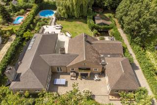 <strong><span>Exclusieve laagbouwvilla op 2.191m² met 4 slpk / 3 bdks en binnen-en buitenzwembad</span></strong><br /><br />Zeer rustig gelegen in een residentiële buurt grenzend aan het Zoerselbos bevindt zich deze uitzonderlijke villa met hoogstaande afwerking en een waaier aan luxevoorzieningen, ingericht door Joris Van Apers.<br /><br />Geniet van ultiem wooncomfort op een prachtige locatie, waar ruimte, ontspanning en verfijning samenkomen. De woning onderging grondige renovaties en uitbreidingen in zowel 1998 als 2010. <br /><br />Inkomhal met toegang tot de ruime L-vormige woonkamer (45m²) op Italiaanse eiken parket met een massieve handgemaakte schouw. Gastentoilet op exclusieve Azul Bahia granieten vloer. <br /><br />De leefkeuken (37m²) is een absolute eyecatcher: een semi-professionele ruimte, uitgerust met o.a. een teppanyaki, wok, friteuse, inductiekookplaat met vijf zones, dubbele dampkappen, professionele kraan, dubbele spoelbak, stoomoven, twee heteluchtovens, een koelcel, twee wijnkoelers, een ontbijttoog en een vermaler. Het werkblad is in stijlvol Marbrinoise. <br /><br />De biljartkamer (39m²) of extra woonkamer op Bourgondische natuursteen is uitgerust met high-end muurbekleding, een open haard en oude Spaanse kasteeldeuren. Deze ruimte is tevens geschikt als praktijkruimte. <br /><br />Via de royale nachthal bereikt u een aparte wasruimte, een vernieuwde badkamer met losstaand ligbad, wastafel, handdoekdroger en 4 slaapkamers. <br />Slpk 1 (18m²) op parket in Italiaanse notelaar met dressing, ensuite badkamer (2010: dubbele wastafel, ligbad, toilet, handdoekdroger) én directe toegang tot een ontspannend en afgesloten terras met vijver en verschillende fonteinen. <br />Slpk 2 (16m²) op parket met dressing en ensuite badkamer met toilet, inloopdouche, wastafel en handdoekdroger. <br />Slpk 3 (14m²) en slpk 4 (18m²) zijn afgewerkt met parket, waarbij slaapkamer 4 beschikt over een ingemaakte kast. <br /><br />Deze villa beschikt over een ruim binnenzwembad met directe toegang via schuifdeuren tot het terras, waar elektrische verwarming en zonnetenten voor extra comfort zorgen. Aansluitend aan het zwembad bevindt zich een wellnessgedeelte met sauna, douche en toilet. <br /><br />Prachtige aangelegde tuin met buitenzwembad en meerdere terrassen. Het perceel is volledig omheind en toegankelijk via een automatische poort. Er zijn meerdere autostaanplaatsen voorzien langs een verlichte oprit, alsook een werkplaats/schuur met zwembad- en vijverinstallatie. <br /><br /><span>Extra:</span> <br />* EPC B <br />* 30 zonnepanelen (2021) met batterij <br />* Warmtepomp buitenzwembad (2025) <br />* CV op stookolie (2012) <br />* Diverse bergzolders <br />* Hobbykelder (66m²) <br />* Drie elektrische zonnetenten <br />* Openhaardschouwen met afzuiging, blaasbalg en timer (rookvrij) <br />* Inbraakwerend dubbel gelaagd dubbele beglazing <br /><br />Elektrische keuring en asbestattest in aanvraag.