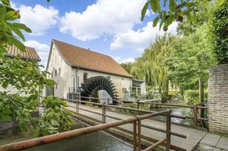 In een pittoresk dorpje ligt verscholen aan de rivier een werkelijk unieke eeuwenoude watermolen. Al rond 1450 werd hier graan gemalen. Het gebouw is geklasseerd historisch erfgoed, opgetrokken uit zo’n 80 cm dik mergelsteen. Waarvandaan u ook kijkt, het weidse uitzicht is werkelijk betoverend en de woonbeleving die u hier vindt is dan ook onevenaarbaar.<br /><br />In 2016 werd het gebouwen met bewoonbare opp. 420 m2 (bruto) van top tot teen gerestaureerd en gemoderniseerd onder auspiciën van twee gerenommeerde architecten. De molen werd weer maalvaardig gemaakt met de nog aanwezige originele tandwielen binnen en een modern efficiënt waterrad buiten. Het fraai ingebouwde, exact passende interieur in werkelijk elke ruimte van het molengebouw, is een creatie van een internationaal geroemde architect in samenwerking met verschillende ontwerpers. De nieuwe daken verzekeren goede isolatie en zijn op twee plaatsen van glas voorzien waardoor de lichtinval optimaal is.<br /><br />Het spel tussen verleden en heden komt overal samen en is tot in perfectie vorm gegeven met de allerbeste materialen. Techniek van topmerken voorziet de gebouwen volkomen onzichtbaar van alle comfort zoals vloerverwarming, mechanische ventilatie en airconditioning, waarbij met veel respect het sfeervolle oude karakter overal in de hoofdrol is gebleven. Voor de fijnere afwerking in o.a. kranen, schakelaars, sanitair en verlichting is gekozen voor high-end designmaterialen.<br /><br />De indrukwekkende maalkamer is nog intact. Wanneer met de molenstenen wordt gemalen is de historische sfeer een ware beleving. Fraai Portugees tegelwerk doet terugdenken aan oude zwartwit geblokte vloeren, een sublieme vondst. De isolatie is voortreffelijk door de dikke mergelsteen, de nieuwe daken en het dubbel-isolerend monumentenglas. Het schrijnwerk is door goede ambachtslui, meesterlijk op maat gemaakt. Iedere luxe slaapkamer met eigen badkamer en toilet heeft een uniek karakter. De grote gezellige leefkeuken vol topkwaliteit apparatuur is om van te dromen. ’s Winters knus bij de houtkachel zitten en ’s zomers op het terras in de verte staren. Het jaar rond is er sfeer en topklasse. En dat alles óók nog eens energie-neutraal! Het majestueuze schoepenrad is hypermodern en van een generator voorzien, zo levert ze de benodigde duurzame elektriciteit. Werkelijk, aan alles is gedacht.<br /><br />Technieken:<br />- Zuppinger waterrad. Betonnen doorvoergoot. Sluizen. Generator, schakelkast en regelaar<br />- Vloerverwarming<br />- Luchtverwarming en airconditioning, regelbaar per ruimte.<br />- Mechanische ventilatie met warmterecuperatie<br />- Warmtepompen (3)<br />- Boilers 2 X 300 liter, water-ontkalker<br />- Regenwater-recuperatie 2 X 4000 liter<br />- Noodverlichting, brand- en rookmelding<br /><br />Indeling:<br />- Molenkamer met historisch molenmechaniek<br />- Steenbed met 2 maalkoppels, luiwerk, werkbank en opslagruimtes<br />- Technische ruimte elektra<br />- Zitkamer met houtkachel<br />- Opkamer met bureel/winkel<br />- Grote leefkeuken met gaggenau-apparatuur<br />- Gewelfde wijnbar/salon met toog en apparatuur.<br />- Voorraadkamer en technische ruimte<br />- Toiletten en wastafel<br />- Wasserij<br />- Moderne aanbouw: eetkamer met apparatuur, daklicht en 2 schuifpuien<br />- Zwevend terras boven het water<br />- 4 karaktervolle slaapkamers, elk met eigen badkamer en toilet.<br /><br />De watermolen is uitermate geschikt als unieke woning, maar biedt ook talloze mogelijkheden voor ondernemende personen. Ze is uitermate geschikt voor hoogwaardige horeca, eten en slapen, een maalderij en winkel ofwel een combinatie van dat alles met wonen en werken. Net zoals voor een bijzondere leefgemeenschap of samengestelde moderne woonvorm. Kortom, u treft hier een werkelijk uniek pand.<br /><br />Geschiedenis:<br />De watermolen kent een rijk verleden. Het oorspronkelijke gebouw dateert vermoedelijk uit de 14e eeuw, waarbij de eerste vermeldingen dateren van 1450. Van weer ruim een eeuw later zijn anekdotes bewaard gebleven vanwege schermutselingen met het garnizoen bij Maastricht. Tussen 1630 en 1650 kende de molen een periode van verval en is de rechter meermalen beslag komen leggen wegens achterstallig onderhoud. Na 1650 kende de molen betere tijden en werd het voorste deel aangebouwd. Aan de vorm van de daken en het niveauverschil binnen is dat nog altijd mooi zichtbaar. Een eeuwenoude gevelsteen geeft een chronogram weer in dichtvorm, uit 1842. Meer dan 5 eeuwen werd hier graan gemalen maar in 1962 werd de molen stilgelegd, verdwenen de sluizen en werd de watertoevoer afgesneden. Het binnenwerk bleef gelukkig bewaard. Een belangrijke erkenning van de historische waarde volgde uiteindelijk in 1981. Sindsdien is de molen beschermd als nationaal monument en zijn de omliggende woningen beschermd dorpsgezicht.<br /><br />De huidige eigenaars beslisten om de watermolen in 2008 te kopen, terug in ere te herstellen en weer maalvaardig te maken. Het ruim 30 meter lange toevoerkanaal langs de molen werd daarvoor opnieuw uitgegraven. Voor een optimaal rendement van de waterkracht werd het kanaal geheel voorzien van een gladde betonnen wand en bodem en kwam er een modern waterrad. In 2016 waren alle renovatiewerken voltooid met een bewonderenswaardig en gelauwerd resultaat. Dit prachtig stuk erfgoed heeft zijn oorspronkelijke bestemming teruggekregen en er werd een nieuwe bestemming aan toegevoegd.<br /><br />Bijkomende informatie:<br />Elektriciteit is conform.<br />EPC Label B - Renovatieplicht niet van toepassing<br />Vastgoed informatie: Vergunning uitgereikt, Woongebied, Geen rechterlijke herstelmaatregel of bestuurlijke maatregel opgelegd, Geen voorkooprecht ruimtelijke ordening aanwezig, Verkavelingsvergunning.<br />Watertoets: P-score: D, G-score: B<br /><br /><br />De ligging:<br /><br />De watermolen ligt aan de uiterste rand van een levendig dorpje, volledig in het groen en tussen de heuvels. Te vinden aan het einde van een doodlopend straatje met aan de voorzijde een pleintje en enkele woonhuizen. Vanuit de voordeur wandelt u rechtstreeks beschermd natuurgebied in, door bos en glooiend landschap, langs rivieren en waterlopen. Er zijn mergelgrotten in de heuvels waar<br />spannende tochten doorheen leiden die vertellen van de historische mergelwinning die deze omgeving beroemd maakte. Hier wonen zo’n 1600 mensen en er zijn gezellige verenigingen, terrassen, een jachthaven, restaurants en een basisschool. Een statig chateau met Michelin-ster ligt om de hoek.<br /><br />De grootste troef van deze omgeving is misschien wel de ligging op de landsgrens van Belgie en Nederland. Op nog geen 5 km. van het hart van één van Nederlands’ mooiste en oudste steden: Maastricht. Waar een ruime keuze is aan (internationale) scholen, een universiteit, academisch ziekenhuis en een rijk cultureel leven. Er zijn talloze musea, boutiques, monumenten en horeca. De wereldberoemde kunstbeurs Tefaf is een jaarlijks terugkerend evenement evenals de openluchtconcerten op het Vrijthof. Maastricht airport en het centraal station zijn goed bereikbaar. Kortom de ligging van deze locatie scoort een dikke 10. Weldadige rust en serene vergezichten rondom en in ruime mate voorzieningen en bruisende levendigheid op wandel- en fietsafstand.
