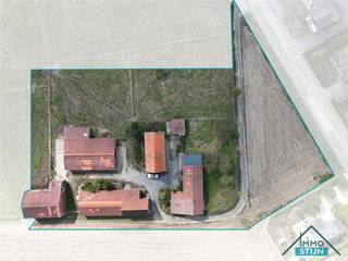 Wie op zoek is naar rust, ruimte en mogelijkheden, vindt hier een bijzonder interessante eigendom. Deze hoeve is zeer rustig gelegen, omgeven door weides en akkers, en combineert het landelijke karakter met een vlotte verbinding naar de E403, diverse winkels en het openbaar vervoer.<br />Via de oprijlaan bereik je de hoeve en de verschillende bijgebouwen. In de woning kom je binnen via een ruime inkomhal die toegang geeft tot twee slaapkamers, de badkamer en de keuken. De badkamer is ingericht met een inloopdouche, lavabo en toilet. De ruime keuken is voorzien van een deels geïnstalleerde keuken en biedt voldoende plaats voor een eettafel met zicht op de binnenplaats en de rest van de hoeve. Vanuit de keuken bereik je de lichtrijke woonkamer, waar plaats is voor een gezellig zitgedeelte, en de praktische berging. Hier bevinden zich onder andere de mazoutbrander en de pomp met filters van de regenwaterput. Vanuit de berging is er toegang tot de droge kelder en leidt de trap naar de vaute en de eerste verdieping. Op deze verdieping bevinden zich nog een derde slaapkamer en een ruime zolder.<br />Buiten vormt de binnenplaats het hart van de hoeve. Rondom bevinden zich een dubbele garage met bovengrondse mazouttank, een tuinberging, twee loodsen en een hoevegebouw met opslagruimte en een voormalige paardenbox.<br />Een belangrijke troef is dat er reeds een definitieve vergunning werd verkregen voor een functiewijziging met behoud van de bestaande gebouwen. Enkel het linkse gebouw bij het oprijden van de binnenplaats dient volgens deze vergunning te worden gesloopt. Samen met de aanwezige weides en gronden biedt deze hoeve heel wat ruimte en mogelijkheden voor wie op zoek is naar een landelijke eigendom met karakter en potentieel. (sted.inl: Vg,Ag,Gmo,Gvkr,Gvv)