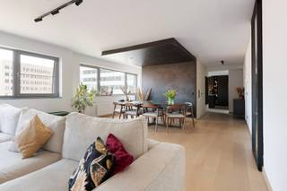 Gelegen op de vierde verdieping en bereikbaar via de lift, betreedt men dit appartement via een verzorgde inkomhal. Deze geeft uit op een ruime leef- en eetruimte met eiken parket. Dankzij de brede gevel en de grote raampartijen geniet de ruimte van veel natuurlijke lichtinval.

Aansluitend bevindt zich de open keuken, visueel gescheiden van de leefruimte door een wand. Zowel de keuken als de inkomhal zijn afgewerkt met een nieuwe beton ciré-vloer. De keuken werd volledig vernieuwd en beschikt over een groot keukeneiland met veel werk- en opbergruimte. De keuken is uitgerust met kwalitatieve toestellen, waaronder een AEG-inductiekookplaat, vaatwasser, combi-oven tot 250°C met zelfreiniging, een Amerikaanse koelkast en een Quooker-kraan. Het werkblad is uitgevoerd in keramiek met travertinlook. Op deze verdieping bevinden zich verder nog een apart gastentoilet en een praktische berging.

Via de trap bereikt men de bovenverdieping. Deze geeft uit op een ruim, zuidwestgericht zonneterras met zicht op het MAS. Op deze verdieping bevinden zich twee slaapkamers, waaronder een ruime masterbedroom met aansluitende dressing, voorzien van maatkasten. Beide slaapkamers zijn uitgerust met airconditioning.

De vernieuwde badkamer beschikt over een inloopdouche, een vrijstaand bad en waskommen in solid surface-materiaal.

Tot slot is er de mogelijkheid om een ondergrondse autostaanplaats aan te kopen, niet inbegrepen in de vraagprijs.