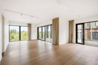 Op de 4e verdieping van het gerenommeerde woonproject Het Kanaal in Wijnegem bevindt zich dit bijzonder lichtrijke appartement met een bewoonbare oppervlakte van ca. 148 m² en een ruim overdekt terras van ca. 32 m². De combinatie van royale raampartijen, een plafondhoogte van bijna drie meter en een hoogwaardige materiaalkeuze zorgt voor een open en verfijnde woonbeleving.<br /><br />Het is mogelijk om hier indien gewenst meerdere slaapkamers te creëren.<br /><br />Het Kanaal vormt een uitzonderlijke woonomgeving waar industrieel erfgoed, hedendaagse architectuur, kunst en landschap samenkomen volgens de visie van Axel Vervoordt. De ligging aan het Albertkanaal biedt een bijzondere setting, terwijl Antwerpen, Schilde en de omliggende gemeenten vlot bereikbaar blijven.<br /><br />Indeling:<br />Het appartement is bereikbaar via de lift en opent in een ruime private inkomhal met vestiaire en geïntegreerde kastenwand. Natuursteen en maatwerk zetten meteen de toon. Aansluitend bevindt zich een afzonderlijk gastentoilet.<br /><br />De royale leefruimte van ca. 50 m² is afgewerkt met parket en wordt aan verschillende zijden omgeven door grote glaspartijen. Hierdoor geniet het interieur van een overvloed aan natuurlijk licht en mooie zichten op de omgeving. Een groot schuifraam geeft rechtstreeks toegang tot het overdekte terras van ca. 32 m², dat een aangename uitbreiding vormt van de woonruimte.<br /><br />Aansluitend bevinden zich de eetkamer van ca. 20 m² en de volledig ingerichte keuken van eveneens ca. 20 m². De keuken is uitgevoerd op natuursteen en voorzien van kwalitatieve inbouwtoestellen, waaronder toestellen van Miele, AEG en Novy.<br /><br />Een polyvalente ruimte van ca. 16 m², momenteel ingericht als dressing, vormt de overgang naar het private slaapgedeelte. De slaapkamer van ca. 16 m² beschikt over parketvloer en toegang tot een balkon.<br /><br />De ruime badkamer van ca. 13 m² is uitgevoerd in Carrara-marmer en voorzien van een vrijstaand ligbad, inloopdouche, dubbel lavabomeubel, handdoekradiator en afzonderlijk toilet. Verder beschikt het appartement over een praktische wasplaats met uitgietbak en technische voorzieningen.<br /><br />Bijzonderheden:<br />- Overdekt terras van ca. 32 m² met zicht op kanaal<br />- Royale plafondhoogte van ca. 2,92 m<br />- Uitzonderlijk veel natuurlijke lichtinval dankzij de grote raampartijen<br />- Royale leefruimte van ca. 50 m²<br />- Polyvalente ruimte, momenteel ingericht als dressing<br />- Lift aanwezig<br />- 2 ondergrondse autostaanplaatsen op niveau -1<br />- Vanuit garage met lift direct toegang tot app<br />- Automatische toegangspoort en videofoon<br />- EPC-label A, 82 kWh/(m² jaar)<br /><br />Unieke ligging binnen Het Kanaal, het internationaal gerenommeerde woon- en kunstproject van Axel Vervoordt