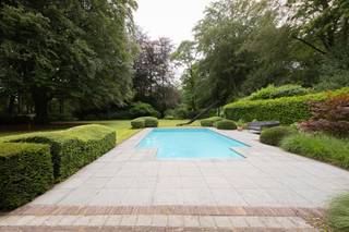 <p><span>Située dans le très prisé quartier de Kapellen-Bos, sur un magnifique terrain orienté sud-ouest d’environ 4.577 m², cette villa d’exception a été récemment rénovée avec un souci du détail remarquable et des matériaux haut de gamme. Elle allie avec élégance le charme intemporel au confort contemporain et bénéficie d’un environnement verdoyant offrant une intimité absolue.</span></p>
<p><span>Dès l’entrée, vous êtes accueilli dans un hall spacieux avec vestiaire et toilettes invités. De superbes portes vitrées en acier mènent à un élégant salon cocktail équipé de meubles sur mesure, qui s’ouvre harmonieusement sur un vaste espace de vie baigné de lumière, agrémenté d’un feu ouvert ainsi que d’un confortable salon et coin télévision. L’espace bureau surélevé constitue une zone de vie supplémentaire offrant de nombreuses possibilités d’aménagement.</span></p>
<p><span>Le cœur de la maison est sans conteste la cuisine familiale luxueusement équipée avec son grand îlot central, ses appareils de qualité supérieure et sa superbe orangerie accueillant la salle à manger. Les larges baies vitrées offrent depuis chaque pièce de vie une vue imprenable sur le jardin paysager et la nature environnante. Une arrière-cuisine entièrement aménagée avec de nombreux espaces de rangement complète cet ensemble. La propriété dispose également d’un double garage intégré.</span></p>
<p><span>À l’étage, la villa propose trois chambres spacieuses. La suite parentale bénéficie de placards intégrés, d’un dressing et d’une élégante salle de bains privative équipée d’une double douche à effet pluie et d’une double vasque. Les deux autres chambres se partagent une seconde salle de bains avec baignoire. Un WC séparé est également présent à cet étage. Un escalier escamotable permet d’accéder à un vaste grenier de rangement occupant toute la largeur de la maison.</span></p>
<p><span>À l’extérieur, vous profiterez d’un magnifique jardin paysager agrémenté d’arbres matures, de plusieurs terrasses ensoleillées ainsi que d’une piscine chauffée avec pompe à chaleur et solar deck. Une élégante dépendance en chêne abrite un carport pour trois véhicules, un local de rangement pour le jardin ainsi que les installations techniques de la piscine. La vaste allée pavée, le double garage intégré et le carport offrent de nombreuses possibilités de stationnement.</span></p>
<p><span>Cette villa prête à emménager se distingue non seulement par son niveau de finition exceptionnel et son caractère unique, mais également par la présence de 24 panneaux solaires avec certificats verts.</span></p>
<p><span>Une propriété exclusive où luxe, confort et sérénité se conjuguent à la perfection.</span></p>