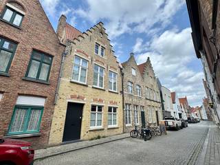 In het gegeerde Guido Gezellekwartier, vlak bij het Engels Klooster, bevindt zich deze charmante en authentieke herenwoning met gezellige stadstuin. Een unieke kans om te wonen op een rustige en mooie locatie, op wandelafstand van de Brugse Vesten en in de onmiddellijke nabijheid van winkels, scholen en openbaar vervoer.
Indeling: ruime inkomhal met ingebouwde kasten en gastentoilet. De prachtige landelijke leefkeuken sluit naadloos aan op de bijzonder ruime leefruimte, ingedeeld in een eetplaats, leeshoek en gezellige zithoek. Dankzij de grote raampartijen geniet deze ruimte van een overvloedige lichtinval en een aangenaam zicht op de stadstuin, die bovendien rechtstreeks toegankelijk is vanuit de leefruimte. De leefruimte wordt extra gekenmerkt door een prachtige parketvloer en een sfeervolle houtkachel.
Op de eerste verdieping bevinden zich twee ruime slaapkamers, waarvan één met dressing, een stijlvolle badkamer uitgerust met een dubbel lavabomeubel, ligbad en inloopdouche, een afzonderlijk toilet en een ruime, praktische wasplaats/berging.
De tweede verdieping, gelegen onder het authentieke gebinte, biedt plaats aan een polyvalente ruimte, een extra slaapkamer met aansluitende dressing en een voorziene ruimte voor een tweede badkamer. De nodige aansluitingen en leidingen zijn reeds aanwezig.
Daarnaast beschikt de woning over een conforme elektrische installatie, een gunstig EPC van 112 kWh/m² (energielabel B), zonnepanelen en airco in de slaapkamers.
Laat u verrassen door de charme, het ruimtegevoel en de centrale ligging van deze unieke stadswoning. 


