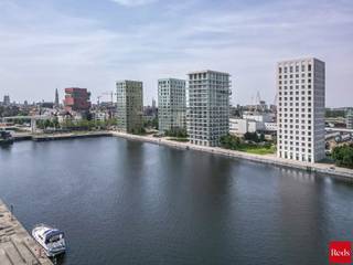 <strong>Stijlvol wonen aan het water – Kattendijkdok Westkaai 51 bus 3.4, Antwerpen</strong><br /><br />Welkom in dit prachtige appartement op een absolute toplocatie aan het bruisende Eilandje. Hier geniet u dagelijks van een uniek uitzicht op het Kattendijkdok, gecombineerd met de levendigheid van de stad, een uitstekende bereikbaarheid en een uitzonderlijke woonkwaliteit.<br /><br />Het gebouw werd ontworpen door de gerenommeerde Zwitserse architect Roger Diener en staat bekend om zijn tijdloze, minimalistische architectuur en hoogwaardige afwerking.<br /><br />Met een bewoonbare oppervlakte van ca. 100 m² biedt dit appartement een perfecte balans tussen ruimte, comfort en elegantie. De ruime leefruimte wordt gekenmerkt door grote raampartijen die zorgen voor een overvloed aan natuurlijk licht en een aangename connectie met de omgeving. Vanuit de leefruimte heeft u toegang tot het westgericht terras, waar u in alle rust kunt genieten van de middag- en avondzon. Het uitzicht combineert het beste van twee werelden: een zicht op het water enerzijds en een levendig stadszicht anderzijds.<br /><br />De open designkeuken is afgewerkt met kwaliteitsmaterialen en uitgerust met hoogwaardige Miele-toestellen, wat garant staat voor optimaal kookcomfort. De leefruimte werd bovendien voorzien van externe zonnewering, waardoor het appartement ook tijdens warme zomerdagen aangenaam blijft.<br /><br />Doorheen vrijwel het volledige appartement werd een kwalitatieve parketvloer doorgetrokken, wat zorgt voor een warme, stijlvolle en uniforme uitstraling. Enkel in de badkamer en het toilet werd gekozen voor een onderhoudsvriendelijke tegelvloer.<br /><br />Het appartement beschikt over twee ruime slaapkamers, een comfortabele badkamer, twee afzonderlijke toiletten en een praktische berging. Dankzij de doordachte indeling is dit appartement uitermate geschikt als gezinswoning, stijlvolle stadswoning of kwalitatieve investering.<br /><br /><strong>Extra troeven:</strong><br /><br />Westgericht terras<br />Zicht op zowel het water als de stad<br />Volledig doorgetrokken parketvloer<br />Hoogwaardige Miele-keukentoestellen<br />Externe zonnewering aan de leefruimte<br />Twee ruime slaapkamers<br />Topligging op het Eilandje<br />Nabij restaurants, musea, winkels en openbaar vervoer<br />Kelderberging en gemeenschappelijke fietsenberging<br />Energiezuinig en voorzien van hedendaags wooncomfort<br /><br />Ondergrondse parkeerplaats verplicht aan te kopen voor €40.000<br /><br />Een uitzonderlijk appartement op een van de meest gegeerde locaties van Antwerpen, waar architectuur, comfort en ligging naadloos samenkomen.<br /><br />Voor meer informatie of een bezoek ter plaatse kan u contact opnemen met Xander via 0497 18 10 84 of xander@reds.be.