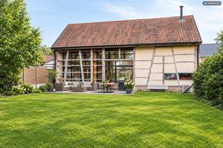 In het hart van het gegeerde Wimmertingen, aan de Luikersteenweg 512, bevindt zich het uitzonderlijke en beschermde pand “Hoeve De Klok” – een uniek gesloten hoevecomplex waar authenticiteit en hedendaags wooncomfort harmonieus samenkomen.<br /><br />Aan de straatzijde bevindt zich het statige poortgebouw met een ruim te renoveren woonhuis. Dankzij de centrale ligging, de vlotte bereikbaarheid en de nabijheid van een ruime parking biedt dit gedeelte tal van mogelijkheden als kantoor, praktijkruimte of extra wooneenheid. Bovendien kan hiervoor een afzonderlijk huisnummer voorzien worden, wat het ideaal maakt voor wie wonen en werken wil combineren.<br />Rond de royale tuin bevinden zich de voormalige vakwerkschuren, die met veel respect voor het erfgoed en oog voor detail werden omgevormd tot een stijlvolle, instapklare woning. Bij de renovatie werd sterk ingezet op energie-efficiëntie en hedendaags comfort, zonder het authentieke karakter van het gebouw uit het oog te verliezen.<br /><br />De woning is uitgerust met vloerverwarming in combinatie met een lucht-waterwarmtepomp, een ventilatiesysteem type C en een geavanceerd domoticasysteem. Ook aan modern wooncomfort werd volop gedacht, met onder meer een laadpaal voor elektrische voertuigen, automatische screens aan de voorgevel en een sfeervolle houthaard als centraal element in de leefruimte.<br />Daarnaast beschikt het pand over regenwaterrecuperatie, een geïntegreerd centraal audiosysteem en een volledig uitgeruste keuken met kwalitatieve inbouwtoestellen. Alles werd afgewerkt met hoogwaardige materialen, waardoor de woning volledig instapklaar is voor wie op zoek is naar een unieke combinatie van comfort en karakter.<br />Op de bovenverdieping bevinden zich momenteel twee ruime slaapkamers, met de mogelijkheid om de indeling eenvoudig uit te breiden of aan te passen aan eigen wensen. Dankzij de doordachte inrichting met lichttracks, programmeerbare verlichting, onzichtbare vloerkanalen en talrijke data-aansluitingen is het pand bijzonder polyvalent.<br /><br />De verschillende gebouwen zijn gegroepeerd rond een sfeervolle, zuidwestgerichte binnenkoer. De ommuring zorgt hier voor een aangenaam microklimaat, ideaal voor een intiem terras of een gezellige binnentuin. Achteraan strekt zich een ruime en rustige tuin uit die grenst aan natuurgebied – een oase van rust en de perfecte uitvalsbasis voor wandelingen in het groen.<br />Bron bewoonbare oppervlakte: EPC.<br /><br />Buitengewone kenmerken:<br />- Vloerverwarming<br />- Wwarmtepomp<br />- Ventilatiesysteem type C<br />- Domoticasysteem<br />- Laadpaal<br />- Automatische screens aan de voorgevel<br />- Branddetectiesysteem met voorbereiding inbraakdetectie<br />- Centraal audiosysteem