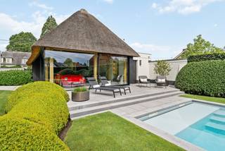 La Ferme Blanche | Luxe intemporelle et savoir-faire exceptionnel<br /><br />Située sur la Hoogstraatsesteenweg à Rijkevorsel, La Ferme Blanche est une propriété exceptionnelle où le luxe intemporel et le savoir-faire sont au cœur de tout. La ferme d'origine de 1931 a été entièrement repensée en 2015 pour devenir une villa élégante de plus de 400 m², finie avec une attention portée aux détails que l'on trouve rarement aujourd'hui. En 2019, le tout a été complété par un poolhouse exclusif, créant ainsi un environnement de vie unique où habiter, se détendre et profiter cohabitent harmonieusement.<br /><br />Dès le premier contact, la qualité exceptionnelle des finitions est évidente. Des matériaux de haute qualité, des aménagements sur mesure raffinés, de la pierre naturelle, des portes intérieures en acier et un éclairage intégré soigneusement créent un ensemble harmonieux où la qualité est palpable dans chaque pièce. De plus, la propriété est impeccablement entretenue et se présente aujourd'hui comme si elle venait d'être réalisée.<br /><br />Située sur une parcelle entièrement clôturée de 1 165 m², vous bénéficiez ici d'une combinaison très agréable de confidentialité, de confort et d'accessibilité. Derrière les portails électriques, un domaine soigneusement aménagé se déploie, où des haies matures, des pelouses parfaitement entretenues et des structures vertes bien pensées créent une atmosphère apaisante et exclusive.<br /><br />En passant par le hall d'entrée, vous entrez dans le cœur de la maison, où les différents espaces de vie se fondent naturellement les uns dans les autres. Grâce aux grandes baies vitrées, chaque pièce bénéficie d'une abondance de lumière naturelle et d'une forte connexion avec le jardin.<br /><br />Le salon chaleureux avec cheminée en bois forme un espace de vie chaleureux et accueillant où le calme et le confort sont au centre de tout. Les grandes baies vitrées offrent une vue magnifique sur le jardin et créent une transition fluide vers la terrasse couverte.<br /><br />Juste à côté se trouve la cuisine intemporelle équipée d'appareils de qualité de marques telles que Miele et Siemens. L'îlot central forme un lieu de rencontre convivial tandis que les plans de travail en granit Jasberg soulignent la finition de qualité de la pièce. Un cellier pratique offre de l'espace supplémentaire pour les appareils de réfrigération et de congélation et facilite l'utilisation quotidienne.<br /><br />Au rez-de-chaussée se trouve également un grand bureau aménagé sur mesure. Grâce à son emplacement calme, cet espace constitue l'endroit idéal pour travailler et vivre en même temps. En outre, le rez-de-chaussée dispose d'une salle de bain avec douche, de toilettes d'invités séparées, d'une buanderie, d'une chaufferie et d'un garage intégré avec point de charge pour véhicules électriques.<br /><br />Par le hall d'escalier, vous accédez à l'étage, entièrement aménagé avec confort et fonctionnalité à l'esprit. Vous y trouverez trois chambres à coucher complètes. Le palier a été équipé d'armoires encastrées qui s'intègrent parfaitement dans l'intérieur. La salle de bain spacieuse est équipée d'un double lavabo, d'une baignoire indépendante et d'une finition de qualité qui s'harmonise parfaitement avec le reste de la maison.<br /><br />Un atout particulier à cet étage est l'immense espace polyvalent. Celui-ci peut être aménagé selon vos envies en salle de jeux, salle de fitness, espace de loisirs, salon supplémentaire ou chambre d'amis. Un escalier escamotable mène également à un grenier séparé, offrant ainsi un espace de rangement pratique.<br /><br />À l'extérieur également, la même norme de qualité sans compromis a été maintenue. La terrasse couverte est une véritable extension de l'espace de vie et offre une vue magnifique sur