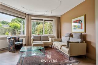 Voor meer info en foto’s, surf naar www.swevers.be – Op een strategische locatie in Tessenderlo-Ham ontdek je deze uitzonderlijk ruime rijwoning met een bewoonbare oppervlakte van 365 m² op een perceel van 8a 75ca. De woning werd oorspronkelijk gebouwd in 1948 maar onderging meerdere renovaties: een nieuw dak (1989), vernieuwde ramen (2015) en een moderne keuken (2018). De gelijkvloerse verdieping biedt o.a. een leefruimte van 50 m², aparte eetkamer, ruime keuken (28,6 m²), badkamer, wasplaats en een garage van 40 m². Daarnaast zijn er praktijkruimtes met aparte ingang, ideaal voor zelfstandigen. Op de eerste verdieping vind je drie grote slaapkamers, een tweede badkamer, apart toilet en een extra kamer die als dressing of bureau kan dienen. De zolderverdieping is volledig ingericht als extra woongedeelte met woonkamer, aansluitingen voor een keuken, slaapkamer of polyvalente ruimte van 55 m², vijfde slaapkamer, zesde slaapkamer of polyvalente ruimte en balkon. Dankzij de zonnepanelen en zonneboiler, gunstige oriëntatie en centrale ligging nabij winkels, scholen en openbaar vervoer, is dit een ideale woning voor grote gezinnen of wie wonen en werken wil combineren. Voor meer informatie, bel 011 255 155. Bron bewoonbare oppervlakte: EPC – verslag.