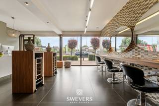 Voor meer info en foto’s, surf naar www.swevers.be – Instapklare commerciële ruimte met uitstekende zichtbaarheid langs de Kempische Steenweg 378 in Hasselt. Deze volledig gerenoveerde handelsruimte van 74 m², gebouwd in 1988 en gelegen op een perceel van 10 are 44 centiare, bevindt zich in een verzorgde staat en is momenteel ingericht als kapsalon. Dankzij de praktische indeling is het pand echter ook geschikt voor tal van andere commerciële of dienstverlenende activiteiten. De open handelsruimte wordt aangevuld met een aparte keuken (8,9 m²), een afzonderlijk toilet en een handige berging (2,9 m²). De aanwezige maatwerkinrichting zorgt voor een professionele uitstraling en laat een nieuwe eigenaar toe om snel van start te gaan. Het pand beschikt over een gunstig EPC-label A, is asbestveilig en heeft lage gemeenschappelijke kosten. Voor de deur zijn publieke parkeerplaatsen beschikbaar. Daarnaast kunnen optioneel twee garageboxen worden aangekocht voor 35.000 euro. Tijdens de renovatie werden onder meer de ramen vernieuwd en werd kwalitatief maatwerk voorzien. De ligging is een absolute troef: op 4,2 km van de autosnelweg, met openbaar vervoer op 300 meter, winkels en scholen op 450 meter en restaurants op 600 meter. Een representatieve handelsruimte met uitstekende bereikbaarheid en maximale visibiliteit, ideaal om uw zaak verder uit te bouwen. Voor meer informatie, bel 011 255 155. Bron bewoonbare oppervlakte: EPC – verslag.