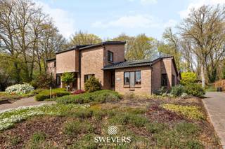 Voor meer info en foto’s, surf naar www.swevers.be – Deze ruime open bebouwing aan de Koerselsesteenweg 146 in Beringen combineert comfortabel wonen met professionele mogelijkheden. Dankzij aparte ingangen voor het privé- en praktijkgedeelte is de woning ideaal voor een zelfstandige activiteit aan huis, maar ook geschikt voor kangoeroewonen. De woning dateert van 1980 en werd doorheen de jaren gericht vernieuwd, met onder meer een nieuw pannendak, gerenoveerde living en keuken, vernieuwde condensatieketel, drie nieuwe Veluxramen en zonnepanelen uit 2023. Met een bewoonbare oppervlakte van 340 m² is er bijzonder veel ruimte. Op het gelijkvloers bevinden zich een woonkamer met eetkamer van samen 46 m², een keuken van 16,40 m², bureau en apart toilet. Het praktijkgedeelte omvat een wachtruimte, consultatieruimte, archief/doka en eigen toilet. Daarnaast zijn er een inpandige garage van 42 m² en een ruime berging. De eerste verdieping telt vier slaapkamers van 12,5 tot 22 m², waarvan één met terras en één met ingemaakte kasten. Verder zijn er een badkamer en apart toilet. De kelder van 44 m² zorgt voor extra bergruimte. Het perceel van 37a 75ca beschikt over een groen aangelegde tuin met meerdere terrassen en tuinhuisjes. Er is parkeerruimte voor 8 à 10 wagens. Scholen, openbaar vervoer en de snelweg zijn vlot bereikbaar. Extra troeven zijn het alarmsysteem, rolluiken, zonnewering en een beveiligde deur. Voor meer informatie, bel 011 255 155. Bron bewoonbare oppervlakte: EPC – verslag.
