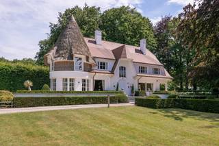 <p><strong>Villa De Maretak – Een stukje geschiedenis in Kapellenbos</strong></p>
<p>Gebouwd in 1911 naar een ontwerp van architect Florent Van Reeth<strong>,</strong> werd Villa De Maretak opgetrokken als buitenverblijf voor de Antwerpse familie Muls. De naam verwijst naar hun stadsvilla "De Maretak" aan het Vleminckveld. Latere renovaties hebben bijgedragen aan het behoud van die rijke geschiedenis en de uitstraling van weleer.</p>
<p>Op een prachtig aangelegd perceel van 16.629 m² vormt deze karaktervolle villa een ware blikvanger. De authentieke architectuur, met de kenmerkende rieten toren, verleent de woning een unieke en tijdloze uitstraling. Rondom geniet u van een volgroeide tuin, een zwembad en een uitzonderlijke ligging aan het water. Een zeldzaam eigendom waar historische charme, ruimte en natuur op een vanzelfsprekende manier samenkomen.De woning verwelkomt u in een royale inkomhal met vide, natuurstenen vloer en een elegante trap die meteen de toon zet. Van hieruit vloeien de leefruimtes op een natuurlijke manier in elkaar over. De salon, met zijn warme parketvloer, houten balkenplafond en open haard, vormt het hart van de woning en geniet dankzij de grote raampartijen van een permanente relatie met de tuin. Aansluitend bevindt zich een tweede leefruimte die zich perfect leent als tv-kamer of familiekamer.</p>
<p>De eetkamer, ondergebracht in de karaktervolle ronde toren, biedt rondom een prachtig uitzicht op het omliggende groen en sluit rechtstreeks aan op de terrassen. De afzonderlijke leefkeuken is praktisch ingericht, geniet van veel natuurlijk licht en vormt een aangename plek voor dagelijks gebruik.</p>
<p>De eerste verdieping werd ingericht met het oog op comfort voor het hele gezin. De masterbedroom, ondergebracht in de karaktervolle toren van de woning, vormt het absolute middelpunt. Dankzij de royale oppervlakte, het ronde grondplan en de ensuite badkamer krijgt deze kamer een heel eigen uitstraling. Verder bevinden zich op deze verdieping nog twee ruime slaapkamers, elk voorzien van een eigen badkamer en rechtstreekse toegang tot een balkon met uitzicht op de tuin. Een doordachte indeling die elke slaapkamer haar eigen comfort en privacy geeft, zonder het familiale karakter van de woning te verliezen.</p>
<p>De woning beschikt ook over een ruime kelder, momenteel ingericht als thuisbioscoop en voorzien van de technische ruimtes.</p>
<p>De zolderverdieping is reeds voorzien van een vierde badkamer en biedt nog de mogelijkheid om twee extra slaapkamers te realiseren. Daarnaast leent deze verdieping zich ook perfect als hobbyruimte, kinderverdieping of thuiskantoor.</p>
<p>De tuin vormt zonder twijfel één van de absolute troeven van dit eigendom. Een doordacht landschapsontwerp combineert perfect onderhouden hagen, volwassen bomen, royale gazons en meerdere terrassen tot een buitenruimte die elk seizoen tot haar recht komt. De verschillende terrassen nodigen uit om op elk moment van de dag te genieten van zon, schaduw en het omliggende groen.</p>
<p>Het perceel strekt zich uit tot aan een idyllische vijver, die de tuin een uitzonderlijke diepte en een parkachtige uitstraling verleent. De garages, ruime oprit met rotonde en zorgvuldig aangelegde buitenruimtes maken het geheel compleet. Een omgeving waar rust, privacy en natuur naadloos samenkomen.<br /><br /></p>
<p>Deze villa combineert de rust van Kapellenbos met een uitstekende bereikbaarheid. De centra van Kapellen en Heide, met hun winkels, scholen en restaurants, bevinden zich op korte afstand. Ook het station van Heide en de belangrijkste verbindingswegen liggen vlakbij, waardoor u geniet van een vlotte verbinding richting Antwerpen, Brussel en Nederland.</p>