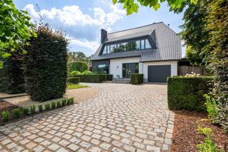 <h3>Energiezuinige villa met luxe afwerking en zonnige tuin (ca. 1.183 m²)</h3>
<p>Deze instapklare villa werd de voorbije jaren grondig gerenoveerd en biedt een perfecte mix van ruimte, comfort en energie-efficiëntie. Denk aan een prachtige uitbouw met overdekt terras, een nieuw dak, zonnepanelen met thuisbatterij, nieuwe gevelisolatie en tal van op maat gemaakte kasten en details. <br /><br /><strong>Gelijkvloers</strong></p>
<ul>
<li><strong>Inkomhal</strong>: Ruime ontvangsthal met gastentoilet. Vernieuwde trap met indirecte verlichting.</li>
<li><strong>Leefruimte</strong>: Sfeervolle en zeer ruime woonkamer, ingedeeld in een zithoek met houtkachel, eetkamer en een bureauhoek in de uitbouw. Grote raampartijen met automatische zonnewering bieden prachtig zicht op de tuin en toegang tot het overdekte terras.</li>
<li><strong>Keuken</strong>: Moderne, volledig uitgeruste open keuken met een geïntegreerde led-tv achter de kookplaat. Via een verborgen deur is er toegang tot een wijnkelder.</li>
<li><strong>Praktische ruimtes</strong>: Achteraan bevinden zich een berging met wasplaats (aparte zij-ingang) en een douchekamer met inloopdouche, lavabo en toilet, ook toegankelijk vanaf het overdekt terras.</li>
</ul>
<p><strong>1e verdieping</strong></p>
<ul>
<li><strong>Hoofdslaapkamer</strong>: Recent vernieuwde ouderslaapkamer met aanpalende dressing. Instant hotelsuite gevoel!</li>
<li><strong>Kinderkamers</strong>: Drie comfortabele slaapkamers, allen voorzien van maatkasten en op maat gemaakt meubilair.</li>
<li><strong>Badkamer</strong>: Luxe badkamer met ligbad, inloopdouche en dubbele lavabo.</li>
<li><strong>Extra</strong>: Nachtal met maatkasten en apart nachttoilet.</li>
</ul>
<p><strong>2e verdieping</strong></p>
<ul>
<li><strong>Zolderkamer</strong>: nachthal met maatkasten en toegang tot de vijfde slaapkamer met ingebouwd bed en extra bergruimte.</li>
<li><strong>Zolderberging</strong></li>
</ul>
<p><strong><br />TUIN</strong></p>
<ul>
<li><strong>Tuin</strong>: Een fraai aangelegde, privacyrijke tuin met voldoende ruimte om te ontspannen en veel zon (ZUID-WEST)</li>
<li><strong>Garage</strong>: Royale dubbele garage met automatische poort, bereikbaar via een naastgelegen straat.</li>
</ul>
<h3><strong>Bijzonderheden</strong></h3>
<ul>
<li><strong>Zonnepanelen</strong>: 19 panelen met thuisbatterij (10 kW).</li>
<li><strong>Klimaatregeling</strong>: Airconditioning in de master bedroom en zolderkamer. Vloerverwarming in combinatie met radiatoren.</li>
<li><strong>Uitbouw</strong>: Voorzien van zonnescreens (2009).</li>
<li><strong>Duurzaamheid</strong>: Nieuw dak, nieuwe gevelisolatie achter crepi, regenwaterput aanwezig.</li>
</ul>
<p>Deze villa combineert energiezuinigheid met een hoogstaande afwerking en is klaar om jou en je gezin te verwelkomen. Mis deze kans niet!</p>