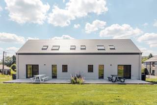 Op enkele minuten van Bastogne, in het hart van Saint-Ode, verenigt dit recente vastgoedcomplex twee geschakelde huizen met elk ongeveer 180 m² woonoppervlakte op een perceel van bijna 2.000 m². Deze configuratie biedt een interessante combinatie van residentieel erfgoed, flexibiliteit in gebruik en verhuurpotentieel.<br /><br />Elke woning biedt een ruime, lichte woonkamer, een volledig uitgeruste keuken, vier slaapkamers en twee badkamers. De leefruimtes komen uit op een terras en een eigen tuin, terwijl een garage met een gemotoriseerde deur elke eenheid completeert. De indeling maakt verschillende erfgoedstrategieën mogelijk: familiebewoning, intergenerationele co-housing of verhuur van beide woningen.<br /><br />Elk huis is voorzien van 12 zonnepanelen, hoogwaardige PVC-ramen, leistenen dakbedekking en een alarmsysteem. Verschillende apparaten zijn op afstand te bedienen. Gelegen in een residentiële en groene omgeving, blijft het complex goed bereikbaar naar Bastogne, voorzieningen en belangrijke wegen. Een zeldzame residentiële configuratie, die de koper de mogelijkheid biedt om een vastgoedportefeuille op te bouwen of te diversifiëren binnen één complex.