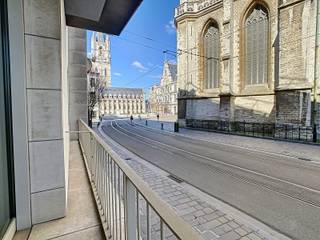<p>Dit bijzonder bel-étage appartement onderscheidt zich door zijn uitzonderlijke ligging in het historische hart van Gent, zijn royale raampartijen en de toegang tot een prachtig aangelegde, zuidgerichte gemeenschappelijke tuin van maar liefst 1.150 m².</p>
<p>Gelegen in de Limburgstraat, op amper enkele stappen van het Sint-Baafsplein, bevindt u zich hier midden in het bruisende stadscentrum, omringd door historische pracht, gezellige horecazaken en een uitgebreid aanbod aan winkels. Vanuit het appartement geniet u van een uniek zicht op zowel de Sint-Baafskathedraal als het Belfort, een zeldzame combinatie die het wonen hier bijzonder maakt. Dankzij de centrale ligging zijn ook openbaar vervoer, belangrijke invalswegen en horeca vlot bereikbaar, wat dit appartement niet alleen aantrekkelijk maakt voor eigen bewoning, maar ook als investering.</p>
<p>Het luxueuze appartementsgebouw werd opgericht in 2007 en straalt kwaliteit en duurzaamheid uit. Het appartement zelf beschikt over een 2 slaapkamers, badkamer met douche, 2 toiletten, en biedt een aangename combinatie van ruimte, licht en flexibiliteit.</p>
<p>Via de lift of enkele trappen bereikt u het appartement, dat toegankelijk is via een gepantserde deur. De inkomhal geeft toegang tot de lichtrijke leefruimte en een polyvalente ruimte die perfect kan dienen als slaapkamer of bureau. De leefruimte vormt één open en indrukwekkend geheel, waarbij de grote raampartijen zorgen voor een overvloed aan natuurlijk licht en een uniek zicht aan beide zijden: enerzijds op de historische stad, anderzijds op de rustige, groene binnentuin.</p>
<p>De multifunctionele kamer kan eenvoudig geïntegreerd worden in de leefruimte dankzij schuifdeuren, waardoor u de indeling volledig kan afstemmen op uw woonbehoeften.</p>
<p>Verder beschikt het appartement over de mogelijkheid tot aankoop van een ondergrondse staanplaats, bereikbaar via een autolift. Daarnaast is er een ruime ondergrondse duplexkelder. Binnen de gemeenschappelijke delen geniet u bovendien van een uitzonderlijk dakterras met een adembenemend uitzicht op de drie torens van Gent.</p>
<p>Een unieke opportuniteit voor wie op zoek is naar comfortabel en stijlvol wonen op een absolute topligging in Gent.</p>