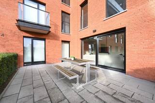 Dit lichtrijk gelijkvloers appartement maakt deel uit van de succesvolle ontwikkeling <em>København</em>. Deze residentie bevindt zich in een wijk die volop in ontwikkeling is en gekenmerkt wordt door nieuwe projecten met een duidelijke opwaardering van de omgeving. Een ligging die het beste van beide werelden combineert: de rust van de Voorhaven en de nabijheid van het stadsleven met vlotte ontsluiting naar de R4 en R40. <br /><br />Het tweeslaapkamer appartement heeft een bewoonbare oppervlakte van 94 m<sup>2</sup> en biedt een zonnig zuidoostelijk gericht terras van liefst 25,8 m<sup>2</sup>. De indeling is als volgt: een inkomhal, een lichtrijke leefruimte ingedeeld in een eet- en zitplaats met rechtstreekse toegang tot het terras en een open keuken. Via de nachthal heeft men toegang tot het toilet, de praktische berging, twee slaapkamers, met beiden toegang tot het terras, en een badkamer voorzien van een inloopdouche en dubbele lavabo.<br /><br />Tot slot dient bij dit appartement een ondergrondse autostaanplaats aangekocht te worden (€ 30.000) en kan men tevens gebruik maken van de gemeenschappelijke fietsenstalling. Het appartement wordt sinds 2024 vlot verhuurd aan een trouwe en correct betalende huurder (€ 1.100/ maand + € 85 provisie gemene lasten). Het appartement wordt verwarmd met radiatoren op aardgas voor een aangename warmte. Daarnaast is het appartement uitgerust met een ventilatiesysteem type C, wat zorgt voor een gezond binnenklimaat.