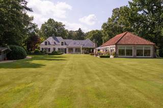 <span>Gelegen in een residentiële laan tussen het centrum van Schilde en ś-Gravenwezel bevindt zich deze exclusieve Vlassak-Verhulst villa op een perceel van 7.637 m2. De ruime Villa beschikt onder meer over een verwarmd binnenzwembad en een volledig afgescheiden appartement dat perfect als kangoeroewoning kan fungeren. De mooi aangelegde tuin is zuidwest gelegen en geniet van een eindeloos zicht op de weilanden. Het perceel is praktisch geheel omheind en dankzij de aangelegde tuinpaden en verlichting wordt er een gevoel van rust en privacy gecreëerd. De inkomhal met klassieke trap, gastentoilet en toegang naar de kelder, annex wijnkelder vind men centraal terug in de woning. Van hieruit bereikt men een woonkamer met statige open haard. Deze kamer is momenteel als biljartruimte en bureau in gebruik. Aan de andere zijde van de woning bevindt zich de TV/zitruimte met prachtig zicht op de tuin. Aansluitend komen we terecht in de open leefruimte. We treffen hier een volledig met luxueuze materialen uitgeruste keuken, een grote eetkamer en een gezellige zitruimte met sfeervolle BARBAS cassette haard en schuifpui naar een prachtig overdekt terras met grote open haard. Verder vinden we beneden nog een wasruimte met berging en een inpandige automatische garage voor twee wagens en ruime parking buiten. Op de eerste verdieping treffen we na de hal eerst en vooral het master bedroom-gedeelte aan. Via een dressing met ingemaakte kasten komen we terecht in het slaapgedeelte en de luxueuze badkamer met o.a. massage-douches. Bovendien is er nog een aparte inloopdressing. Verder beschikt de eerste verdieping over een aparte leefruimte met open keuken/leefruimte, een zeer ruime slaapkamer en een badkamer. Boven één van de slaapkamers is er een toegang naar de zolder waar zich de Viessmann gasverwarming bevindt. Het bijgebouw uit 2010 bestaat uit een volledig geautomatiseerd onderloop zwembad prachtig afgewerkt met mozaiek. Deze ruimte geniet van een schitterend uitzicht over de tuin en de aanpalende weilanden. Verder vinden we in het bijgebouw nog een sauna en een infrarood sauna en een volwaardige badkamer. De giga kelder van het bijgebouw werd enerzijds ingedeeld als technische ruimte voor het zwembad en anderzijds als werkplaats en bergruimte.</span>