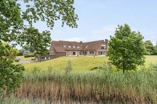 Omringd door weidse graslanden ligt deze imposante villa, een woning die rust en ruimte op een vanzelfsprekende manier met elkaar verzoent. Wie hier thuiskomt, laat de drukte achter zich: het domein ligt aan een oude arm van de Leie genaamd "Oude Leiebedding", met rietkragen en water die het geheel een serene, bijna tijdloze sfeer geven.<br /><br />De woning is opgetrokken in een warme baksteenarchitectuur onder een markant pannendak, met de allure van een landhuis dat gebouwd is om generaties mee te gaan.<br /><br />Binnen wordt die klasse meteen voelbaar. De inkomhal zet de toon met authentieke baksteen en Bourgondische natuursteen als vloer, met vloerverwarming.<br /><br />De leefruimtes zijn royaal en licht. Grote schuiframen lopen over de volledige breedte en openen zich naar meerdere terrassen en de tuin, zodat het landschap als het ware deel wordt van het interieur. Een open haard en een natuurstenen schouw zorgen voor warmte en gezelligheid in de wintermaanden. De ruime, afgewerkte keuken met natuurstenen werkbladen sluit naadloos aan op de leefruimtes.<br /><br />Comfort wordt hier ruim ingevuld: de woning beschikt over een verwarmd binnenzwembad onder een sfeervol houten gewelf met grote glaspartijen die uitkijken op het groen, een plek om het hele jaar door van te genieten.<br /><br />De slaapvertrekken zijn uitzonderlijk ruim. De master bedroom op het gelijkvloers kijkt via een eigen terras uit over de omliggende velden en beschikt over een dressing en een aansluitende badkamer. Daarnaast biedt het eerste verdiep, dat toegankelijk is via een lift, 2 royale slaap- en badkamers, evenals een grote, polyvalente ruimte. Perfect voor gasten, een home gym, game room of extra thuiskantoor.<br /><br />Kortom: een uitzonderlijk eigendom voor wie houdt van klassieke elegantie, kwalitatieve materialen en bovenal ruimte en privacy, zonder in te boeten op comfort.