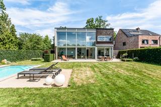 Deze moderne vrijstaande woning op de grens met Brasschaat in de Claessensdreef is rustig gelegen, vlak bij het groen van de Kattekensberg, en toch op amper vijf minuten van het centrum van Brasschaat en Kapellen. <br /><br />Bij het binnenkomen kom je in een ruime inkomhal. Rechts vindt u een gastentoilet en een aparte vestiaire. Verder in de gang richting de leefruimte is er een toffe bureauruimte op de linkerkant discreet weggewerkt.<br /><br />Recht voor u opent de woning zich in een lichtrijke leefruimte met open keuken. De vide tot aan het dak boven het salon geeft een gevoel van ruimte. de achtergevel, bijna volledig in glas, haalt de zuidelijke tuin naar binnen. Bovendien zijn alle ramen aan de achterzijde voorzien van zonnewering. Naast de leefruimte ligt een sfeervolle extra kamer, vandaag gebruikt als tv- en leeshoek. Een doorkijkhaard verbindt beide ruimtes visueel, en zorgt voor extra gezelligheid op koude avonden. <br /><br />De open keuken sluit aan op een praktische aparte berging, met rechtstreekse toegang tot de inpandige garage met elektrische poort. <br /><br />Via de inkomhal leidt de trap naar de eerste verdieping, waar u drie ruime slaapkamers vindt waarvan 2 voorzien van airco, twee badkamers en een aparte wasberging. Eén slaapkamer beschikt over een eigen dressing en ensuite badkamer.<br /><br />Buiten wacht een groot perceel. Vooraan een ruime oprit met plaats voor minstens 4 wagens, achteraan een prachtige, private tuin die de hele dag zon vangt dankzij de zuidoriëntatie. Het recent vernieuwd, verwarmbare ingebouwde zwembad vormt zonder twijfel de blikvanger van deze buitenruimte.<br /><br />Bijzonderheden:<br />- EPC C<br />- Elektriciteit conform<br />- Zonnepanelen<br />- Bamboe parket<br />- Vloerverwarming<br /><br />Attesten (EPC, EK) zijn beschikbaar via onze website: https://jamar.immo/<br />Wg – Vg – Gvkr – Gvv – Gmo – Geen overstromingsgevoelig gebied – Geen Worg