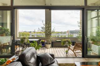 Wonen op een stukje Gentse geschiedenis, vertaald naar hedendaagse architectuur. Op de voormalige gasfabrieksite, staat nu dit indrukwekkende appartement (163m²) te koop. Het omringende park, ontworpen door Denis Dujardin rond de historische gashouders, biedt een rustige, groene oase op wandelafstand van de bruisende binnenstad. Een ongeëvenaarde toplocatie die rust combineert met een vlotte bereikbaarheid.<br /><br />Binnenkomen is een absolute beleving. De uitzonderlijke hoge plafonds en kamerbrede raampartijen trekken het daglicht rijkelijk naar binnen en onthullen een majestueus zicht op de iconische torens van Gent. De hoogwaardige afwerking springt onmiddellijk in het oog: de imposante tegels van 1,2 meter creëren een naadloze, weelderige basis die pure luxe ademt.<br /><br />De royale leefruimte vloeit prachtig over in het ruime, zuidwest-gerichte terras. Oorspronkelijk voorzien van drie slaapkamers, is het grondplan doordacht aangepast naar twee volwaardige slaapkamers en een stijlvolle open bureauruimte, perfect afgestemd op de moderne levensstijl.<br /><br />Naast het unieke wooncomfort tilt het gebouw uw levenskwaliteit nog hoger dankzij een exclusieve inpandige gemeenschappelijke fitness. Dit is resideren waar licht, ruimte en geschiedenis perfect in balans zijn.<br /><br />Het aankopen van 2 staanplaatsen in het gebouw is ook een optie. <br /><br />Interesse? Contacteer ons voor een bezoek ter plaatse. <br /><br />Bestuursmaatregelen in het maatregelenregister: nee