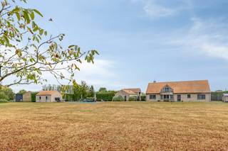 Tussen het groen in Zwevezele, op een riant domein van 10.997 m², biedt deze instapklare eigendom uit 2006 een uitzonderlijk totaalpakket voor wie riant wil wonen én professioneel wil ondernemen. De locatie garandeert rust en privacy, gecombineerd met een vlotte aansluiting richting Torhout, Roeselare en de E403. <br /><br />Het huis verrast door een indrukwekkende lichtinval, doordachte ruimtes en een hoogwaardige afwerking. Het gelijkvloers omvat een royale leefruimte met sfeervolle haard, een volledig uitgeruste leefkeuken met bijkeuken en koelcel, een bureau, drie slaapkamers en een ruime badkamer. Boven bevindt zich een extra woongedeelte — voorzien van een leefruimte, keuken, zonneterras, badkamer, dressing en twee extra slaapkamers. Deze indeling leent zich ideaal voor kangoeroewonen, een gastenverblijf of een praktijk.<br /><br />Buiten treft u een hoogwaardig aangelegde tuin waar rust en privacy centraal staan. Het uitnodigende zwembad, de jacuzzi en de sfeervolle vijver vormen samen het hart van het domein, met op de achtergrond een prachtig, vrij uitzicht over de omliggende velden. Het  bijgebouw — compleet ingericht met een sauna en inloopdouche — tilt het comfort op eigen terrein naar een nog hoger niveau. Een heerlijke plek om in volledige discretie te ontspannen en van het buitenleven te genieten.<br /><br />Voor zelfstandigen of ondernemers zijn de logistieke voorzieningen ongewoon uitgebreid op eigen terrein: een ruime hoofdloods, een tweede loods met dubbele doorrijpoort, overdekte opslagruimtes, een dubbele garage en drie garageboxen. Bovendien is de eigendom toekomstgericht uitgerust met een milieuvriendelijke warmtepomp, 58 zonnepanelen en 60.000 liter regenwateropslag.<br /><br />Bestuursmaatregelen in het maatregelenregister: nee