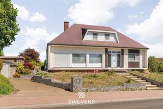 Voor meer info en foto’s, surf naar www.swevers.be – In Halen, aan Kauwplasstraat 55, vind je deze instapklare woning met veel ruimte, licht en een aangename groene omgeving. De woning werd gebouwd in 1963, is verzorgd onderhouden en biedt een bewoonbare oppervlakte van 221 m² op een perceel van 12a 51ca. Op het gelijkvloers geniet je van een ruime leefruimte van 40 m² met zithoek en eethoek. Dankzij de grote raampartijen voelt deze ruimte open en licht aan. De praktische keuken van 16 m² sluit mooi aan op het dagelijkse wooncomfort, terwijl de veranda extra leefruimte biedt met zicht op de tuin. Verder zijn er op deze verdieping drie slaapkamers van 20 m², 16 m² en 13 m², samen met de badkamer. De eerste verdieping telt nog twee bijkomende slaapkamers van elk 12 m². Deze kamers zijn ideaal als kinderkamer, logeerkamer, hobbyruimte of bureau. De woning beschikt daarnaast over een ruime kelder van 68 m² wat tal van opbergmogelijkheden biedt. Daarnaast zijn er twee bijgebouwen aanwezig, namelijk een tuinhuis en een garage, elk met een oppervlakte van ongeveer 21 m². De noordoostelijk georiënteerde tuin biedt een groen en agrarich uitzicht zonder directe bebouwing aan beide zijden en vormt een rustige plek om buiten te genieten. Ook de ligging is praktisch: winkels en een bushalte bevinden zich op 800 meter, scholen op 3 km en de snelweg op 3,6 km. Met vijf slaapkamers, veel bergruimte, een ruime garage en een aangename tuin is dit een comfortabele gezinswoning met tal van mogelijkheden. De woning beschikt over een EPC-label C, waardoor er geen renovatieplicht van toepassing is. Daarnaast zijn er 15 zonnepanelen aanwezig, wat bijdraagt tot de energiezuinigheid van de woning. Ook de elektriciteit werd volledig vernieuwd en zal nog door de eigenaars worden gekeurd. Voor meer informatie, bel 012 699 900. Bron bewoonbare oppervlakte: EPC – verslag. De vermelde oppervlaktes zijn louter indicatief. Swevers Real Estate kan niet aansprakelijk worden gesteld voor eventuele onjuistheden in de verstrekte gegevens.