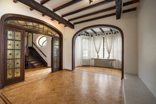 Achter deze klassieke villa uit de jaren '20 schuilt geen gewone woning, maar een thuis waar ruimte, rust en karakter samenkomen. De woning werd gebouwd op een perceel van 9a17ca en via de imposante inkomhal met monumentale houten trap en glas-in-loodramen betreed je een interieur dat meteen verrast. De sierlijke boogdoorgangen, zware balkenplafonds en sfeervolle open haard getuigen van een tijdperk waarin huizen met vakmanschap werden gebouwd.<br /><br />Door de open woonkamer met sfeervolle haard kom je terecht in een volledig ingerichte keuken die uitkijkt op het zuidelijk terras en toegang geeft tot de vrije tuin. De natuurlijke beplanting en hoge bomen zorgen voor een unieke sfeer bij elk seizoen. Een bijzonder pluspunt: via de achtertuin is het park van Strombeek-Bever rechtstreeks bereikbaar — voor de eigenaars één van de redenen om destijds voor deze woning te kiezen. De tuin beschikt daarnaast over een jacuzzi en een groot tuinhuis, wat het buitenleven compleet maakt.<br /><br />Op de eerste verdieping bevinden zich drie slaapkamers (22, 18 en 13 m²) en een dressing. De badkamer met hoekwhirlpool, douche en dubbele lavabo is privatief voor de ouderlijke slaapkamer. Op de dakverdieping vindt u nog twee ruime slaapkamers (18 en 14 m²), elk met de karaktervolle houten afwerking die deze verdieping zo bijzonder maken. Op elk verdiep is een apart toilet en douche voorzien — een doordacht comfort voor het hele gezin.<br /><br />Op tuinniveau bevindt zich een grote bureau- en hobbyruimte van circa 60 m², ideaal als home office of voor een inwonend familielid. De woning is daarnaast voorzien van zonnepanelen (72 m²), een thuisbatterij en wordt verwarmd door een combinatie van een condenserende gasketel en warmtepomp. EPC: E