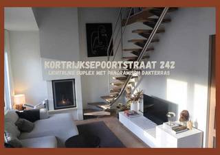 Dit instapklare appartement combineert moderne architectuur met rust, overvloedig licht en een uitzicht over de stad en het water. Bij het binnenstappen van de inkomhal ervaart u direct de rust door de combinatie van lichtrijke kleuren en de warme parketvloer die in het volledige appartement is doorgetrokken. De leefruimte is een absolute eyecatcher door de gashaard en het unieke ruimtegevoel dankzij het hoge plafond. De moderne, greeploze keuken is voorzien van hoogwaardige ATAG-toestellen. De eerste slaapkamer is een serene ruimte met een uitgebreide wand aan op maat gemaakte inbouwkasten. De tweede slaapkamer (mezzanine) op de bovenverdieping biedt een veelzijdige ruimte met een ingebouwd bureau, en beschikt over airconditioning voor een optimaal klimaat het hele jaar door. Praktisch gemak is voorzien door de aparte wasruimte en een gedeelde (fietsen)berging met een aparte ingang. Buiten wacht een oase van rust op het riante dakterras met een panoramisch zicht.<br /><br />De centrale toplocatie van het appartement biedt de ideale balans tussen het bruisende stadsleven en een vlotte verbinding naar het station en de belangrijke invalswegen. Dankzij de Leie direct achter het gebouw en de nabijheid van onder andere de Bijloke-site, de Watersportbaan en de Blaarmeersen, is de rust van water en omliggend groen nooit veraf.<br /><br />Interesse?<br />- Bezoekdagen op 17, 18 en 19 april<br />- Voor het inplannen van een bezoek of vragen: kortrijksepoortstraat242@gmail.com<br />- Er kan geboden worden onder gesloten envelop tot en met woensdag 22 april 2026