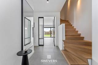 Voor meer info en foto’s, surf naar www.swevers.be – In een rustige woonomgeving in Leopoldsburg bevindt zich deze indrukwekkende open bebouwing uit 2020. Deze instapklare BEN-villa combineert hedendaagse architectuur met ruimte, comfort en een hoogwaardige afwerking. Met een bewoonbare oppervlakte van 298 m² en een perceel van 8a 26ca biedt deze woning een aangename woonbeleving met veel natuurlijk licht dankzij de grote raampartijen. Via de inkomhal betreedt u het gelijkvloers met gastentoilet en een praktische bureauruimte, ideaal voor thuiswerk. De ruime leefruimte van circa 50 m² vormt het hart van de woning en biedt plaats voor een gezellige zithoek en eetruimte. Aansluitend bevindt zich de moderne keuken van ongeveer 24 m² met kookeiland, perfect voor wie graag kookt en gasten ontvangt. Verder zijn er op dit niveau een berging en extra bergruimte aanwezig. De eerste verdieping is ingericht als slaapverdieping met vier ruime slaapkamers van ongeveer 18 m², 20 m², 22 m² en 22,5 m². Daarnaast zijn er twee badkamers en een aparte dressing voorzien, wat extra comfort biedt voor een gezin. Op de tweede verdieping bevindt zich een vijfde slaapkamer van circa 22,5 m², ideaal als logeerkamer, hobbyruimte of bureau, samen met een praktische wasruimte. Rondom de woning ligt een aangename tuin waar u in alle rust kan genieten van het buitenleven. De open bebouwing zorgt voor een ruimtelijk gevoel en extra privacy. Verder beschikt de woning over een garage. Ook de ligging is bijzonder gunstig: scholen op 120 meter, openbaar vervoer op 160 meter en winkels, restaurants en ontspanning op ongeveer 200 meter. De snelwegen zijn bereikbaar op 7,5 km. Voor meer informatie, bel 011 255 155. Bron bewoonbare oppervlakte: EPC – verslag.