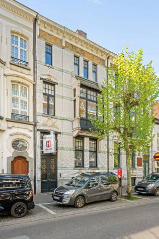 Bij het betreden van deze statige woning naar de hand van architect Jules Taeymans word je meteen verwelkomd in een indrukwekkende inkomhal die naadloos overgaat in een karaktervolle traphal. Op deze verdieping bevinden zich een recent vernieuwde keuken (Interieurstudio Hoskens), een sfeervol salon met hoge plafonds en verfijnde ornamenten, een ruime eetkamer en een lichtrijke tuinkamer die uitkijkt op de tuin.<br /><br />Daarnaast is er een polyvalente hobby- of kantoorruimte met apart sanitair en sauna, rechtstreeks toegankelijk via de inkomhal – ideaal voor ontspanning of professioneel gebruik. Aansluitend vind je de technische ruimte met o.a. de omvormer van de zonnepanelen en de centrale verwarming.<br /><br />Buiten geniet je van een zonnig terras, een gezellige stadstuin en rechtstreekse toegang tot de dubbele garage.<br /><br />Op de verdiepingen bevinden zich maar liefst 7 volwaardige slaapkamers met houten vloeren en 2 badkamers. Deze woning leent zich perfect voor grote gezinnen, co-housing, een combinatie van wonen en werken, of voor wie ruim en comfortabel in het hart van de stad wil wonen.<br /><br />Deze unieke herenwoning biedt uitzonderlijk veel mogelijkheden, zowel voor privébewoning als voor de inrichting van een kantoor of praktijkruimte.<br /><br />Buitengewone troeven:<br />* Tijdloze architectuur gecombineerd met hedendaags comfort, inclusief een dubbele garage met uitrit naar de Molenstraat – een absolute meerwaarde in deze buurt<br />* Energiezuinig dankzij zonnepanelen (2010), conforme elektrische keuring en quasi asbestvrij (enkel één radiatorknop in een slaapkamer)<br />* Centrale ligging nabij winkels, horeca en openbaar vervoer