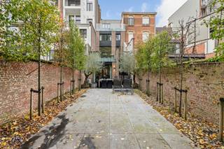 Aan de statige Jan Van Rijswijcklaan in Antwerpen prijkt dit sublieme herenhuis in Neo-Lodewijk XVI-stijl, een architecturaal juweel ontworpen door Edward Van Not in 1912, een naam die synoniem staat voor verfijning, symmetrie en onmiskenbare grandeur.<br /><br />Achter de sierlijke, evenwichtige gevel ontvouwt zich een woning waar ambacht, elegantie en comfort samensmelten tot een zeldzaam harmonisch geheel. Elk detail, van de hoge plafonds met lijstwerk tot de authentieke parketvloeren en marmeren open haarden, ademt karakter en verfijning.<br /><br />De leefruimtes baden in licht dankzij de hoge ramen en creëren een sfeer van stille luxe: groots, maar nooit overdreven. De indrukwekkende leefkeuken vormt het kloppend hart van de woning, een plek waar gastronomie en gezelligheid elkaar ontmoeten. De afwerking is ronduit uitzonderlijk: een Lacanche gasfornuis met teppanyaki-plaat, oven, magnetron, afzuigkap, koelkast met vriesvak en ingebouwde koffiemachine, allemaal samengebracht op een natuurstenen vloer die klasse uitstraalt.<br /><br />Vanuit de keuken kijkt u uit op een onderhoudsvriendelijke stadstuin, met een uniek en open zicht op het groene Hertogenpark, een zeldzaam privilege in het hart van de stad. Hier heerst een rust die contrasteert met de levendigheid van Antwerpen, slechts enkele minuten verderop.<br /><br />Op de tussenverdieping bevindt zich een intieme tv-ruimte met bar en toegang tot een groot betegeld terras van ca. 45 m², ideaal voor avonden in goed gezelschap, met een glas wijn en de stad zachtjes op de achtergrond.<br /><br />De slaapverdiepingen bieden ruimte en sereniteit: twee master suites met eigen dressing en luxueuze marmeren badkamers, aangevuld met vier extra slaapkamers, waarvan twee eveneens voorzien zijn van een eigen badkamer. Overal voelt men de doordachte indeling en het vakmanschap van een tijd waarin huizen nog met trots werden gebouwd.<br /><br />De woning is volledig onderkelderd en herbergt onder meer een wijnkelder, een subtiele knipoog naar levensgenieters die weten te waarderen wat echt goed is.<br /><br />Bijzonderheden<br />+ Terrassen en ramen achtergevel vernieuwd in 2023<br />+ Overal warmtepompen Lucht-Lucht<br />+ Alarmsysteem rechtstreeks verbonden met de politie<br />+ Luxueuze renovatie met topmaterialen<br />+ Volledig onderkelderd met wijnkelder<br />+ Mogelijkheid tot huren van autostaanplaats en garagebox<br /> 