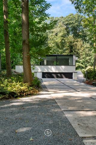 Deze moderne villa uit 2018 is discreet gelegen op een mooi perceel van 2.461 m². De woning en tuin liggen dieper op het perceel, bereikbaar via een lange oprit en afgesloten door een automatische poort. Hierdoor ontstaat een bijzonder private woonomgeving, omgeven door groen en volwassen bomen.<br /><br />De strakke architectuur werd ontworpen met veel aandacht voor licht, ruimte en het contact met de omgeving. De royale leef- en eetruimte bevinden zich op het gelijkvloers en bieden rondom zicht op het groen. Ook de keuken sluit hier mooi op aan en beschikt over een ruime en praktische keukenberging. Het interieur werd bovendien recent volledig herschilderd.<br /><br />De woning telt 340 m² bewoonbare oppervlakte en beschikt over vier slaapkamers, waarvan één momenteel als bureel is ingericht. De ruime master suite beschikt over een eigen ensuite badkamer, terwijl voor de overige kamers een afzonderlijke douchekamer voorzien is.<br /><br />De slaapkamers, badkamers, berging, ruime garage, technische ruimte en wasruimte bevinden zich gedeeltelijk onder het maaiveld. Deze bijzondere indeling zorgt ervoor dat de leefruimtes maximaal van het daglicht en de groene omgeving genieten, terwijl de lagergelegen ruimtes ook tijdens warme zomerdagen aangenaam koel blijven.<br /><br />Ook energetisch is de woning volledig mee met haar tijd, met zonnepanelen, een E-peil van E54 en EPC-label A. Een hedendaagse villa waar strakke architectuur, privacy, groen en modern wooncomfort op een serene manier samenkomen.