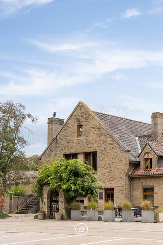 Deze statige villa is gelegen op een toplocatie en beschikt over ca. 575 m² bewoonbare oppervlakte, wat tal van mogelijkheden biedt voor zowel privé- als professioneel gebruik. Dankzij de royale oppervlaktes, veelzijdige indeling en professionele uitrusting leent het pand zich onder meer voor horecafaciliteiten, een combinatie van wonen en werken, een kangoeroeconcept of een andere invulling op maat.<br /><br />Momenteel is de villa als volgt ingedeeld:<br /><br />Op het gelijkvloers bevindt zich een ruime polyvalente ruimte, aangevuld met gastentoiletten, een grote professionele keuken en praktische stockagevoorzieningen.<br /><br />De eerste verdieping omvat opnieuw een ruime polyvalente ruimte, die naar wens verder kan worden ingericht met meerdere slaapkamers en badkamers. Daarnaast bevindt zich hier een volwaardig apart appartement, bestaande uit een slaapkamer, badkamer, uitgeruste keuken en leefruimte.<br /><br />Een ruim balkon biedt bovendien een aangename buitenruimte en vormt een mooie verbinding met de groene omgeving. Rondom de villa bevindt zich een verzorgde tuin met vijver, die de eigendom een bijzondere charme en rust geeft.<br /><br />Verder beschikt deze woning over een dubbele garage en ruime oprit. <br /><br />De combinatie van de uitzonderlijke oppervlakte, de flexibele indeling, het ruime balkon en de aangename tuin met vijver maakt van deze eigendom een veelzijdig geheel met tal van mogelijkheden voor wie op zoek is naar een karaktervolle en ruime eigendom met potentieel.