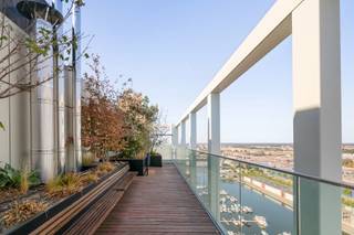 Op een unieke locatie aan het Kempisch Dok bevindt zich op de 22ste verdieping van de iconische Doktoren dit uitzonderlijke penthouse van ca. 132 m². Dankzij de ligging op de hoogste woonverdiepingen en de oriëntatie over drie zijden geniet u van indrukwekkende vergezichten, met als absolute blikvanger het frontale zicht over het Kempisch Dok en de Antwerpse skyline.
De inkomhal beschikt over een gastentoilet en geeft toegang tot de master bedroom met aangrenzend terras en elegante ensuite badkamer met lavabomeubel, inloopdouche en toilet. Daarnaast is er een praktische technische/wasruimte.
De lichtrijke leefruimte wordt gekenmerkt door kamerhoge beglazing en een open keuken die volledig geïnstalleerd is. Vanuit de leefruimte bereikt u het tweede terras, dat volledig met beglazing kan worden afgesloten en zo dienstdoet als aangenaam winterterras.
Aan de andere zijde bevinden zich twee bijkomende slaapkamers waarvan één momenteel als bureauruimte wordt gebruikt en ideaal is als home office. Een tweede badkamer met lavabomeubel en inloopdouche en een afzonderlijk toilet vervolledigen dit niveau.
Het appartement beschikt over vloerverwarming en privatieve zonnepanelen. Op de 23ste verdieping kunnen bewoners bovendien genieten van een gemeenschappelijk dakterras met een uniek panorama over Antwerpen en het omliggende waterlandschap.
Inclusief privatieve kelderberging. Een ondergrondse autostaanplaats dient verplicht bij aangekocht te worden voor € 40.000.